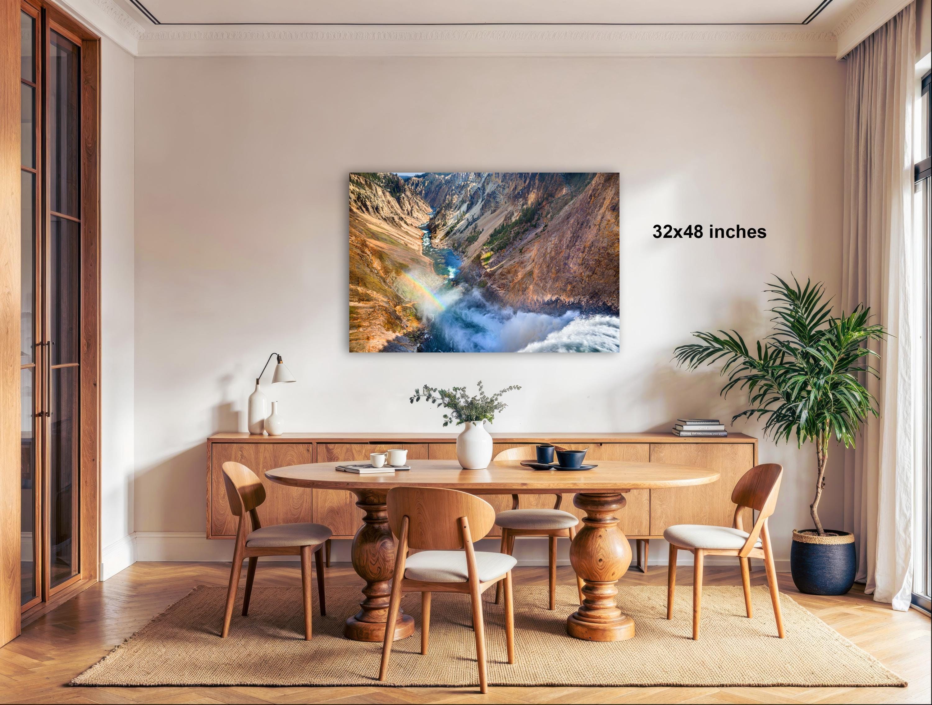 a modern dining room with a large wooden table surrounded by matching chairs. A large framed landscape photograph hangs on the wall above the table, adding a natural element to the room. The room is decorated with a potted plant, a vase, and a lamp, creating a cozy and inviting atmosphere.