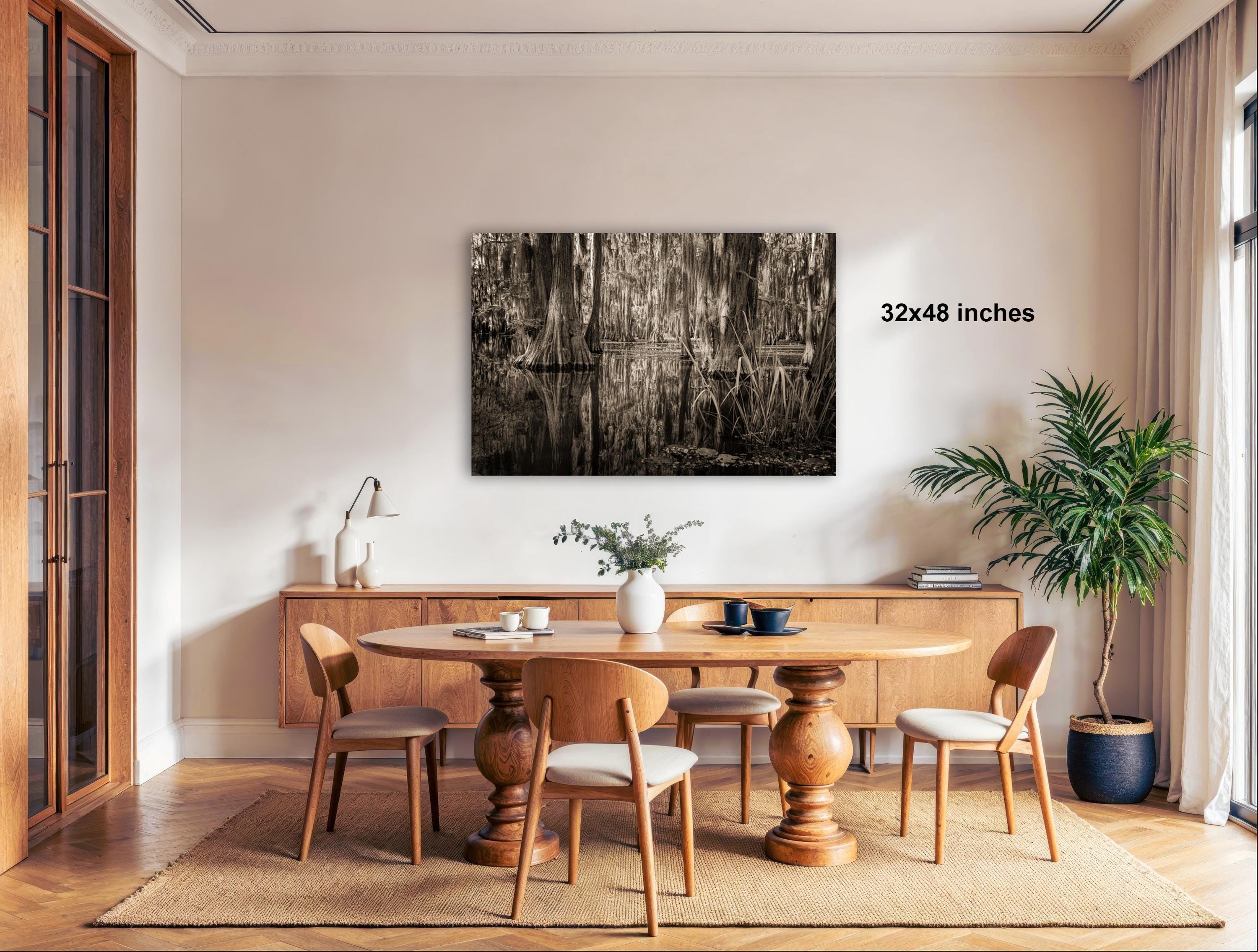 a modern dining room with a wooden table and chairs, a large black and white photograph hanging on the wall, and a potted plant on the right side.