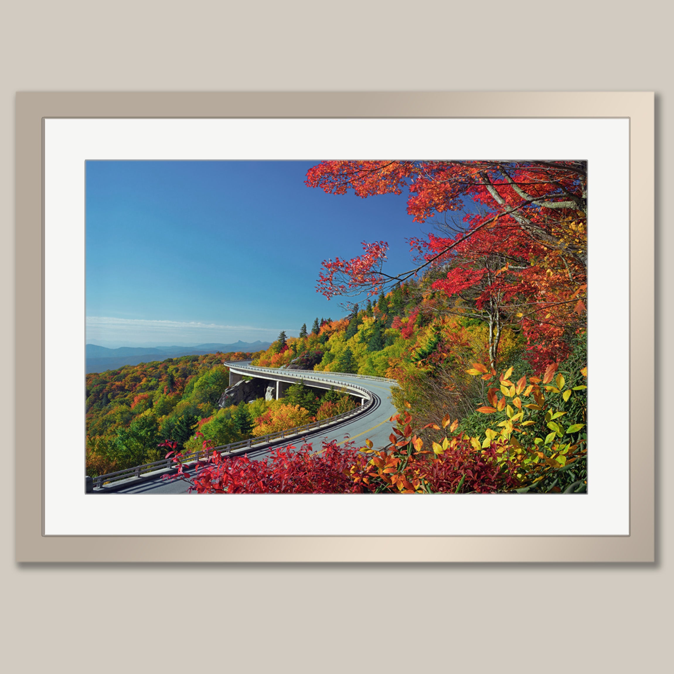 A framed photograph depicting a winding road surrounded by a vibrant autumn landscape, with colorful foliage and a clear blue sky.