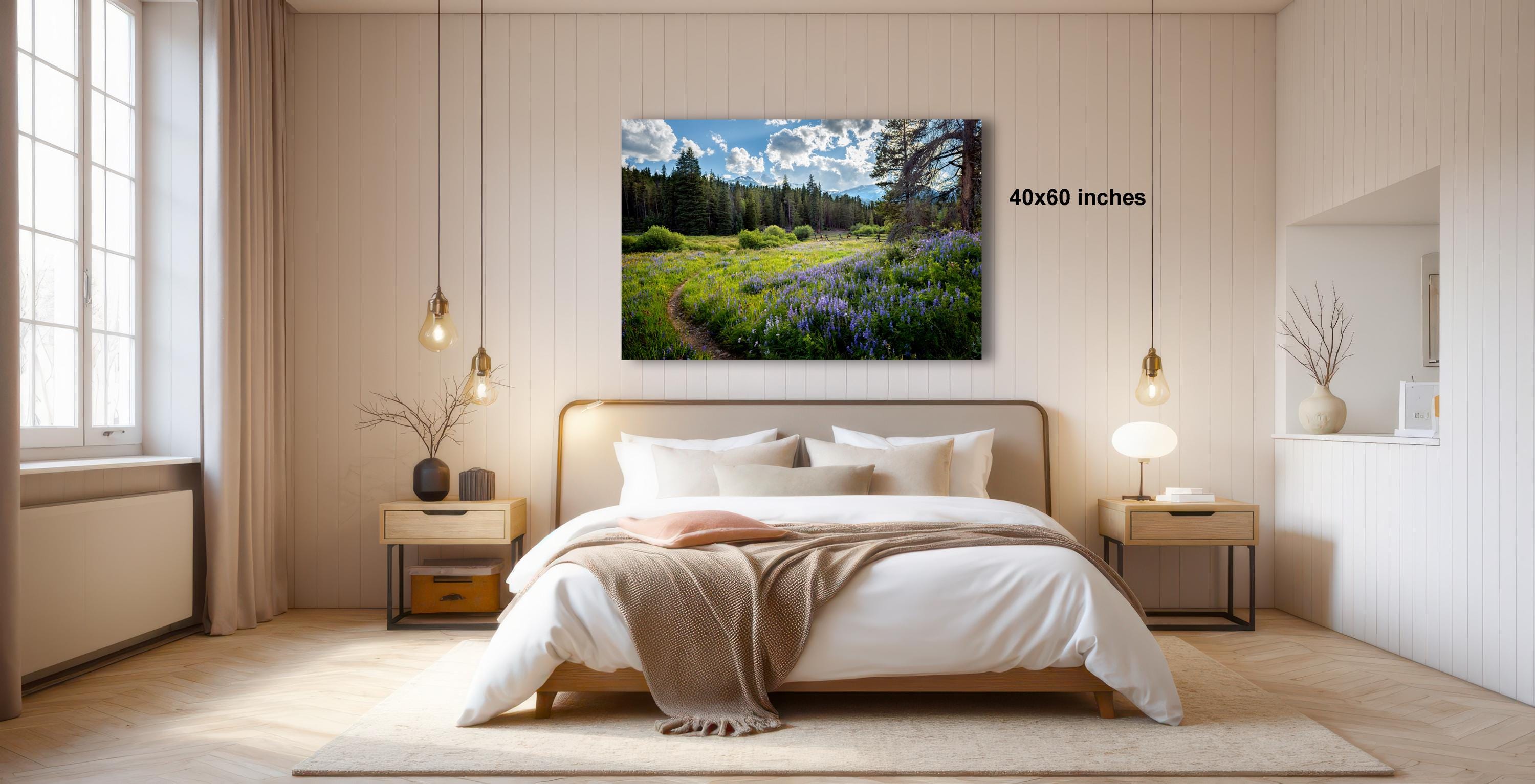 a serene bedroom with a large bed, wooden furniture, and a painting of a field with purple flowers hanging above it.