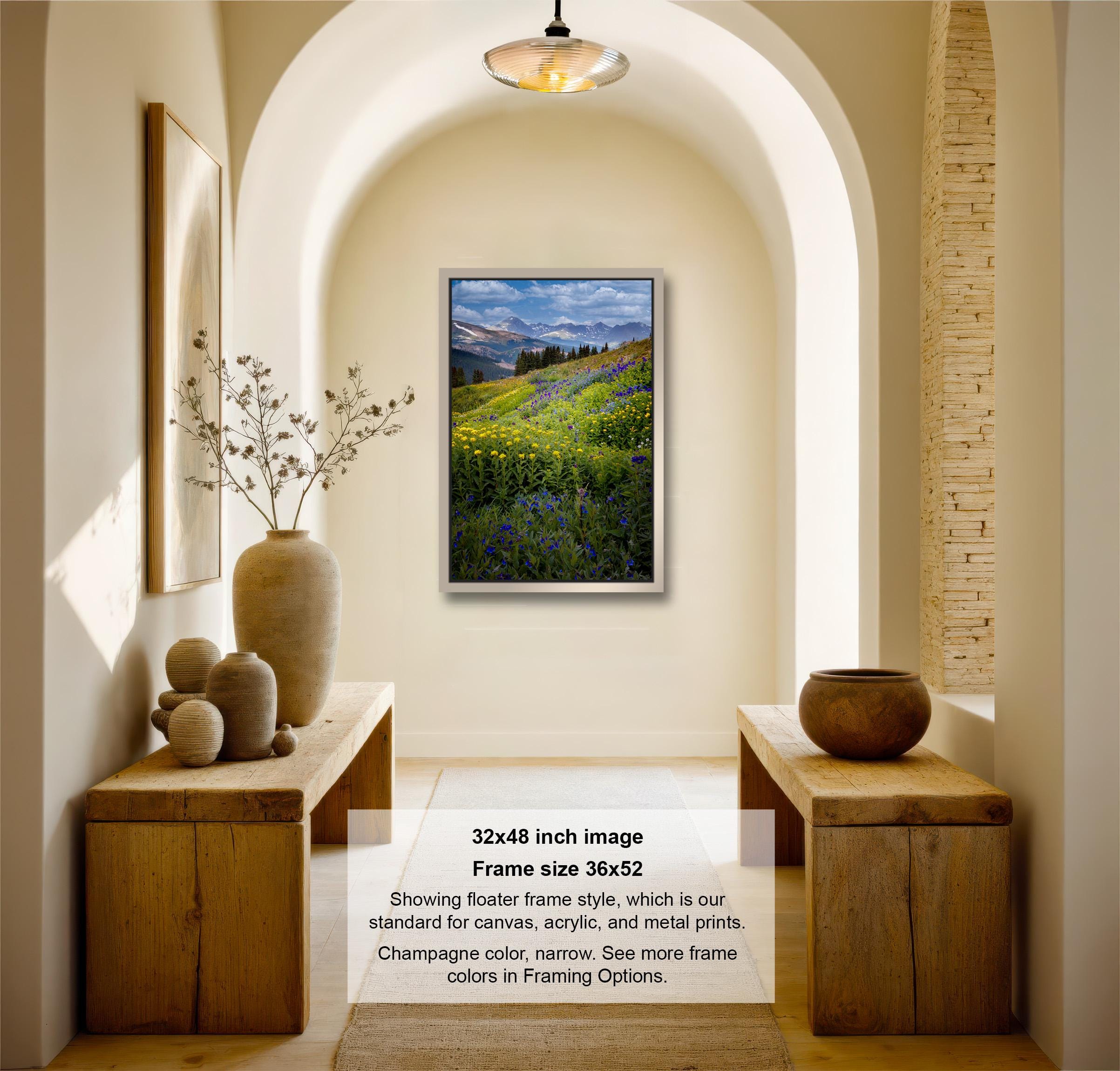 The image is a 32x48-inch framed photograph of a field of flowers, hanging on a wall in a room with wooden furniture and decorative items.