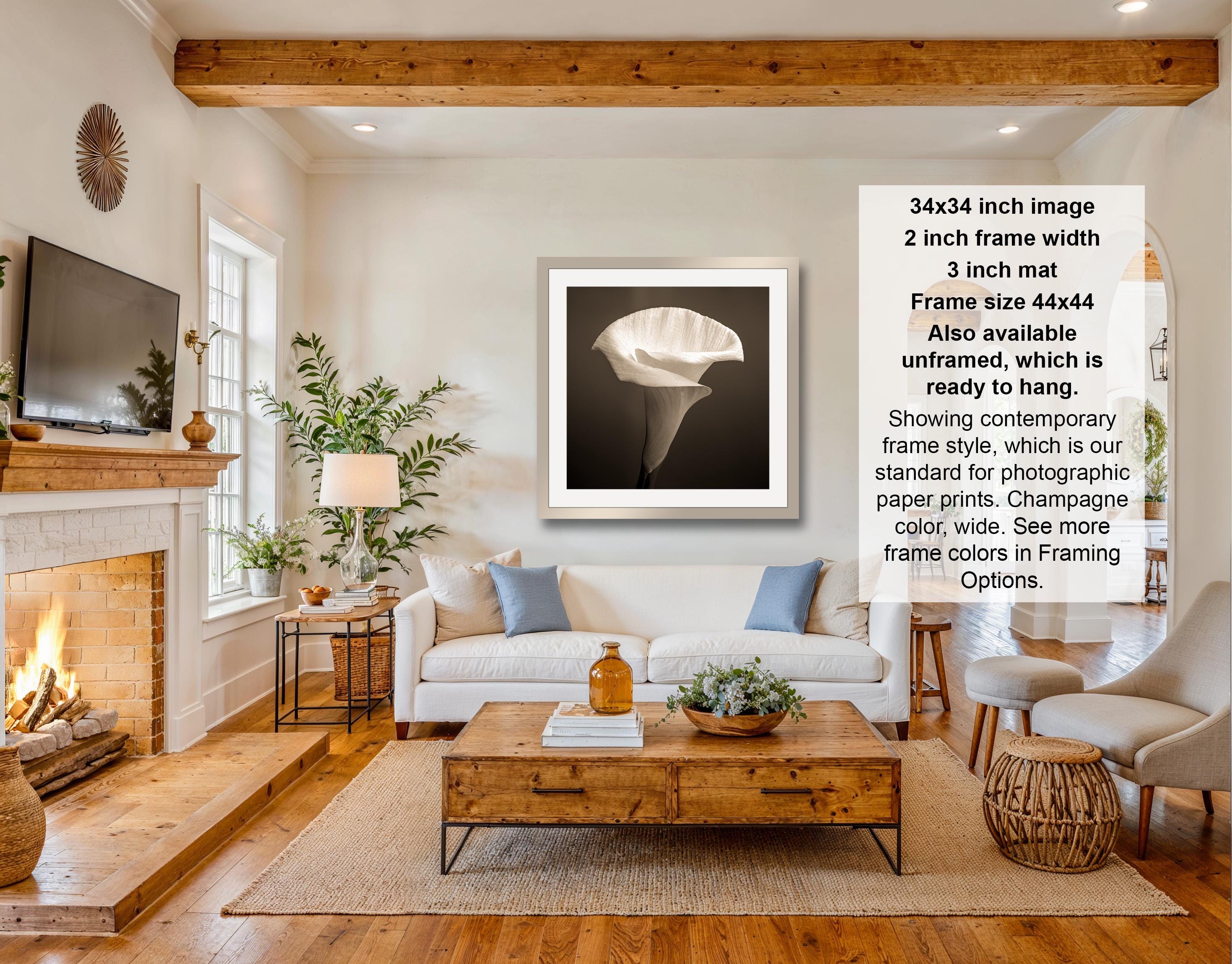 The image is a living room with a fireplace, a white sofa, a wooden coffee table, and a framed photograph of a white flower hanging on the wall.