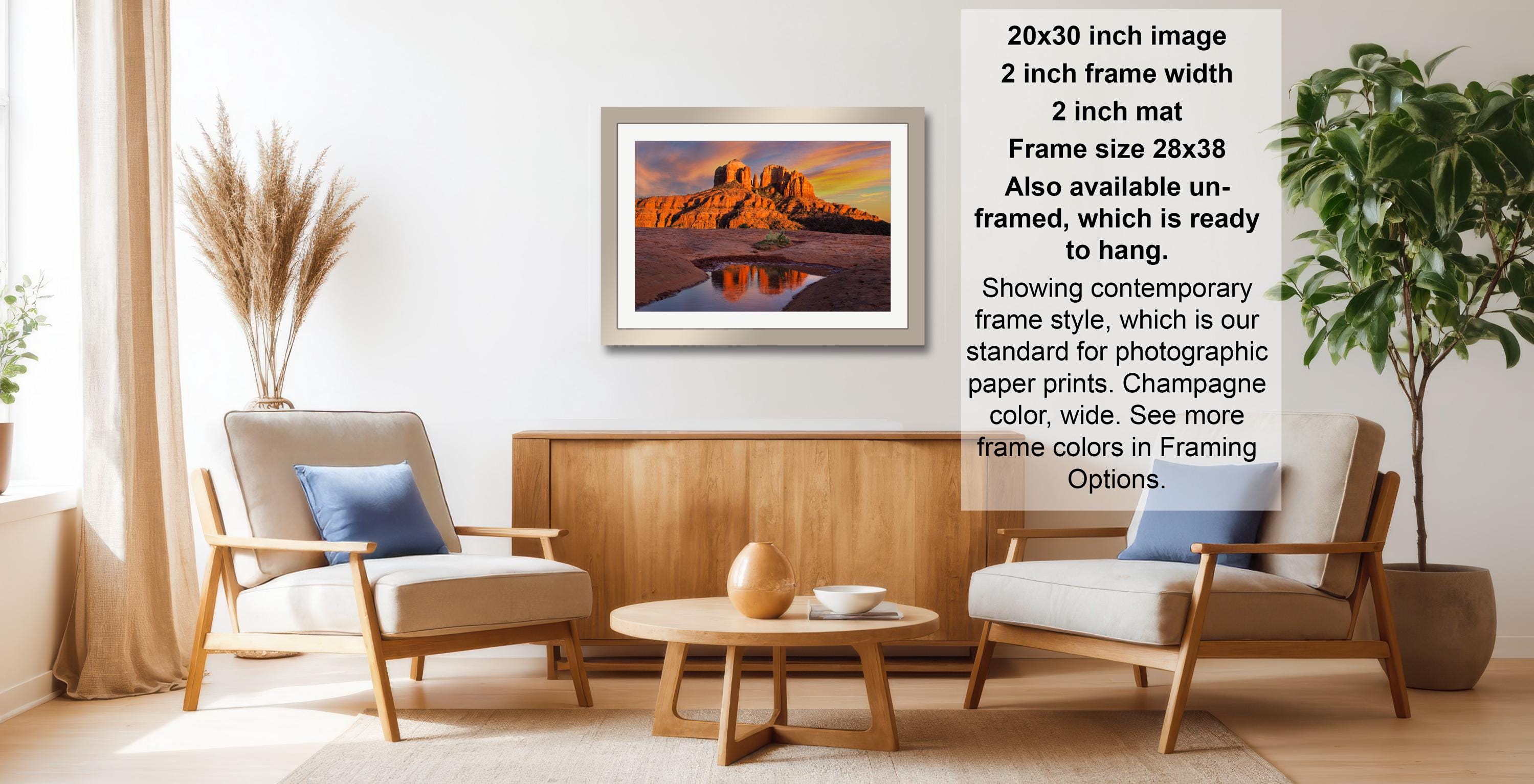 a living room with a framed landscape photograph hanging on the wall, a wooden coffee table in the center, and two chairs facing each other.