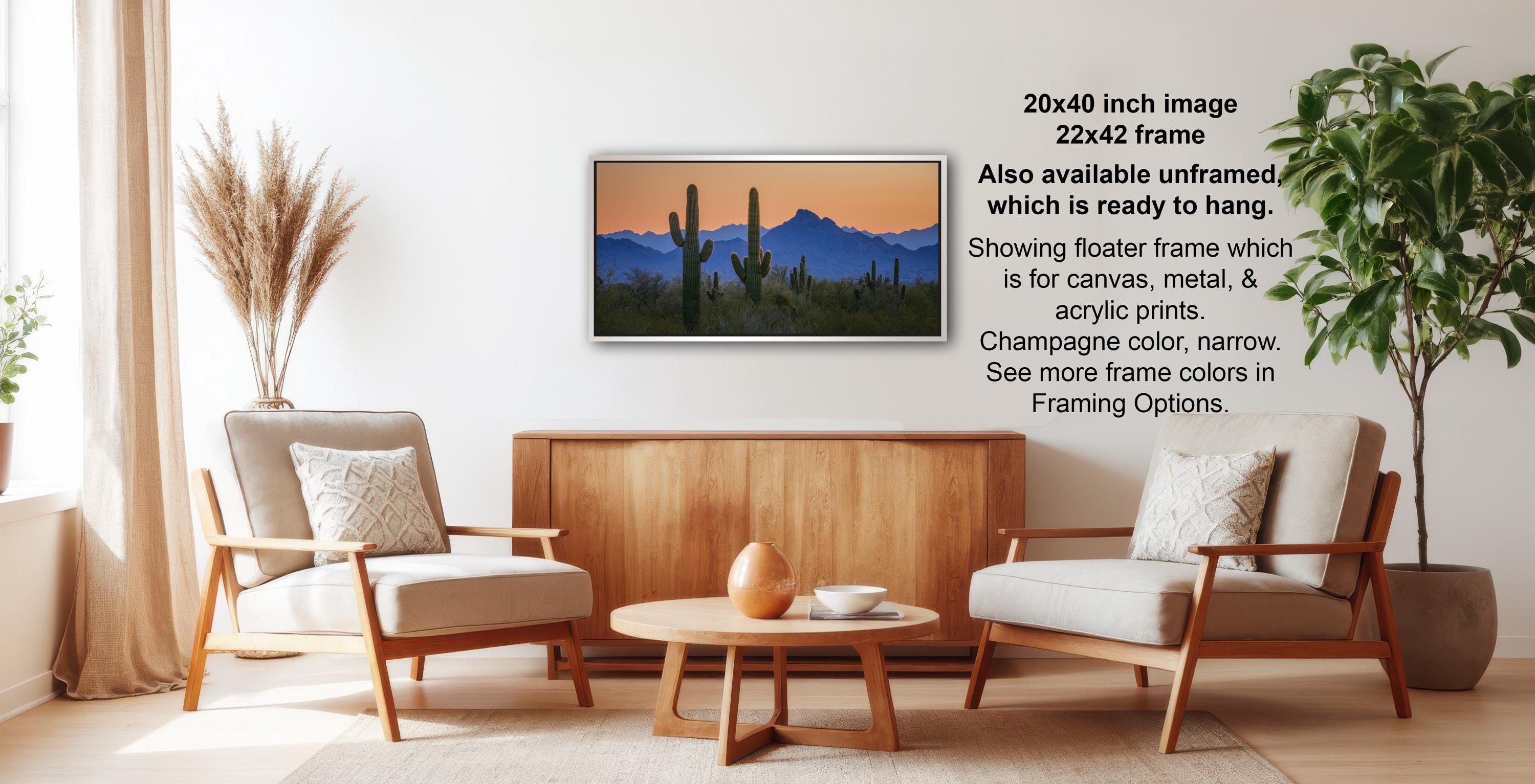 a living room with a wooden coffee table, two white armchairs, and a framed landscape painting of a desert scene hanging on the wall.