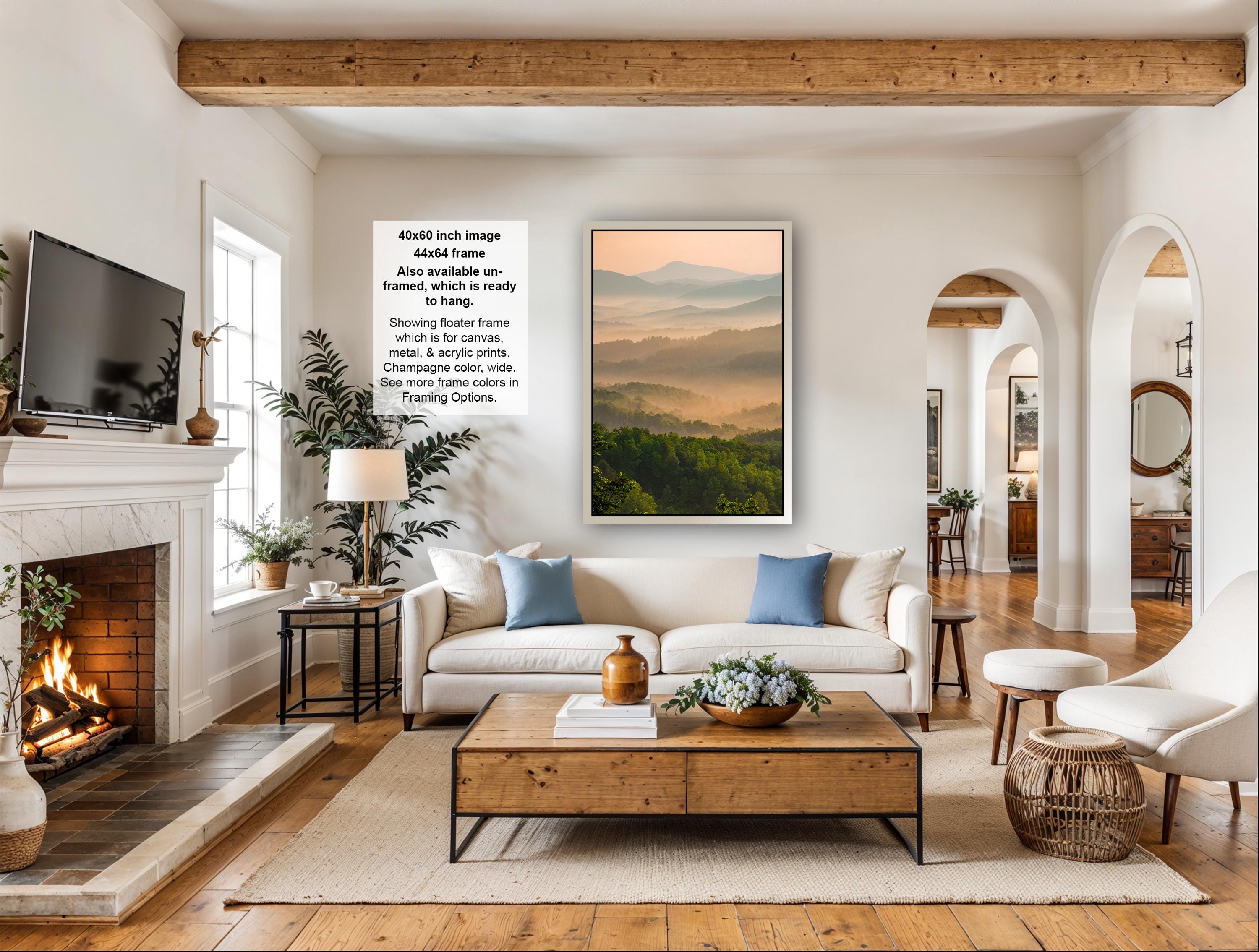 a cozy living room with a fireplace, a large framed landscape painting, a white sofa, a coffee table, and various decorative elements such as potted plants and vases.