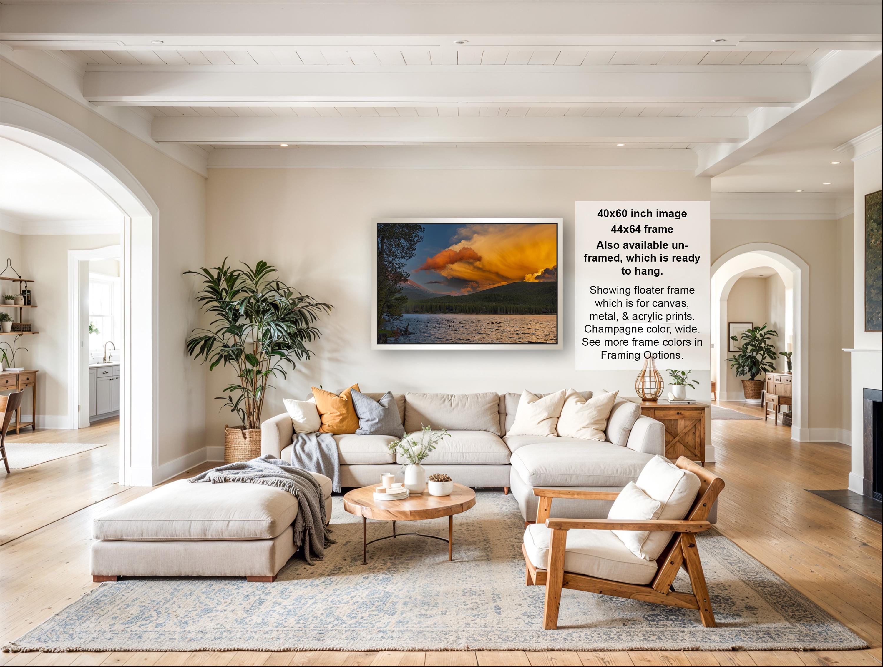 The image is a large, framed picture of a sunset over a body of water, hanging on a wall in a living room.