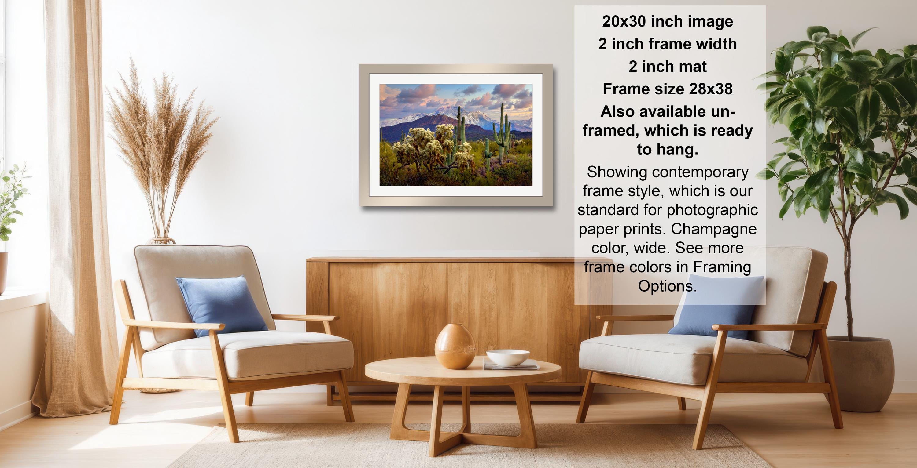 The image is a living room with a framed landscape painting hanging on the wall, a wooden coffee table in the center, and two chairs facing each other.