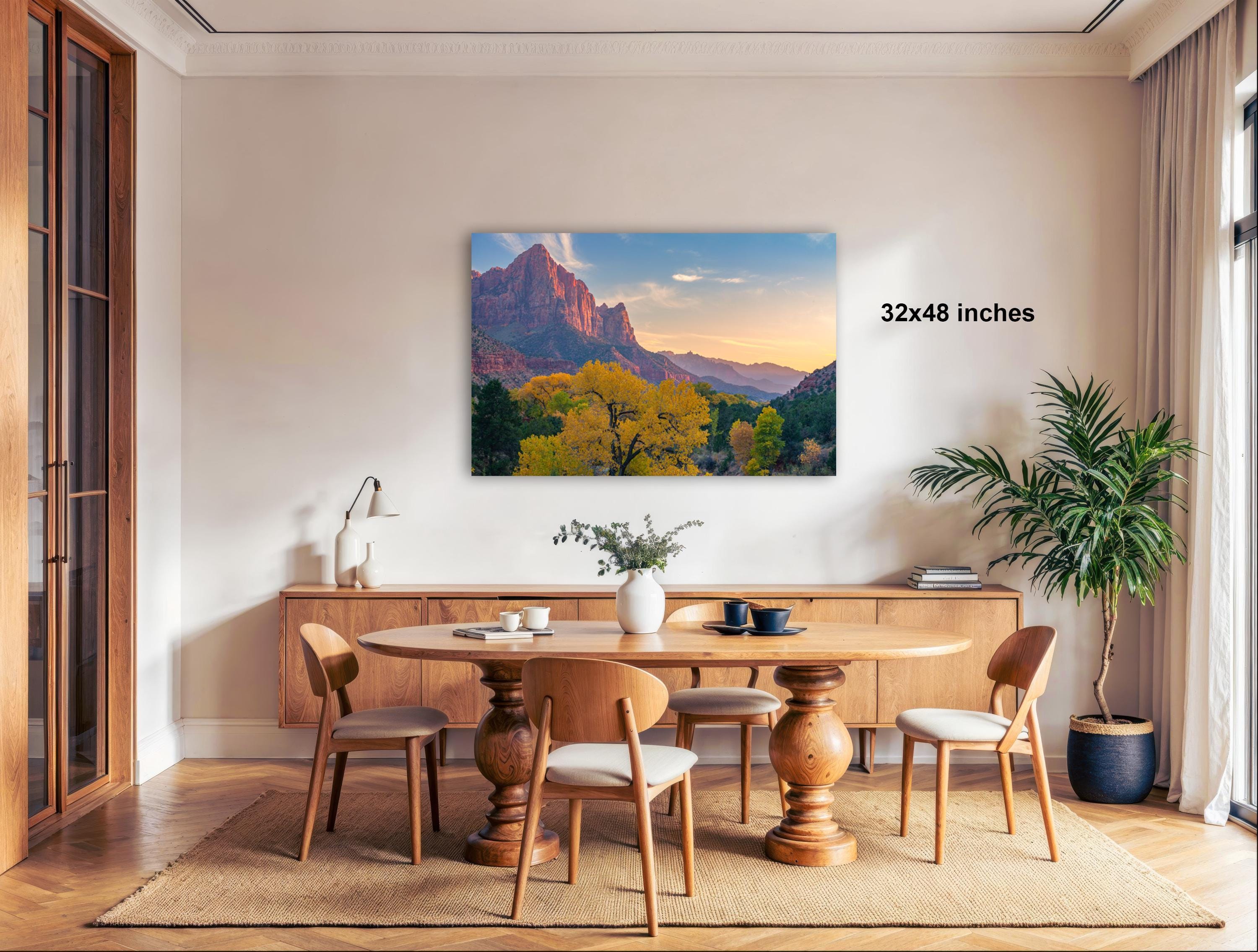 a dining room with a large wooden table surrounded by chairs, a vase of flowers, and a painting of a mountain landscape hanging on the wall.
