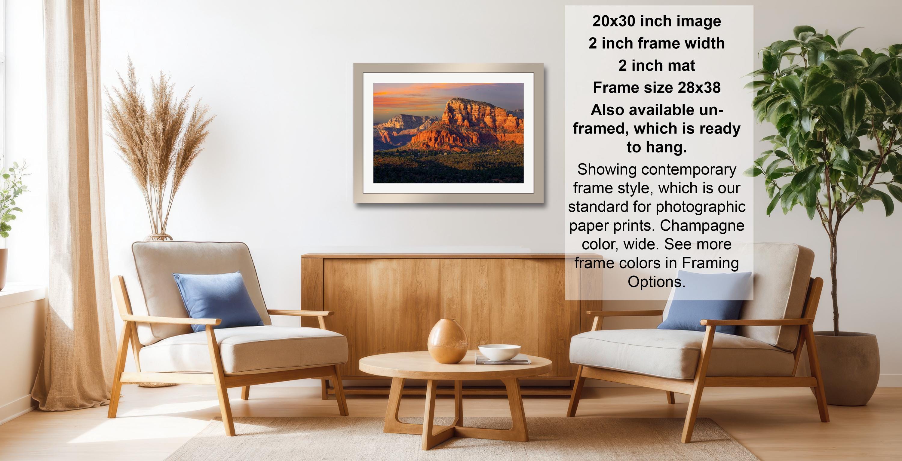 a living room with a framed landscape photograph hanging on the wall, a wooden coffee table in the center, and two chairs facing each other.