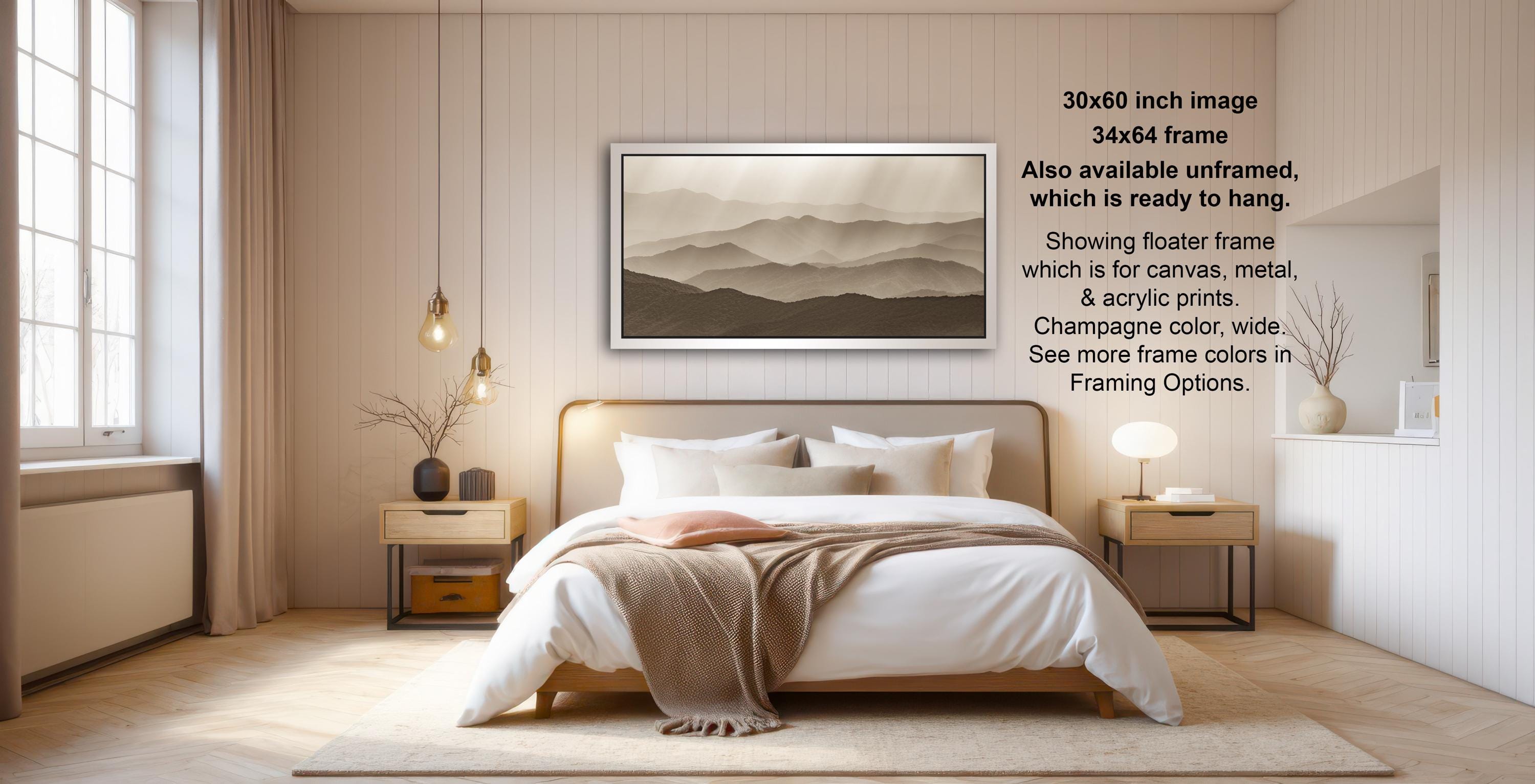 The image is a modern bedroom with a large bed, wooden furniture, and a framed landscape painting on the wall. The painting features a mountainous landscape with a hazy, atmospheric effect. The room has a minimalist and clean design, with a neutral color palette and a touch of natural elements like a potted plant and a vase.