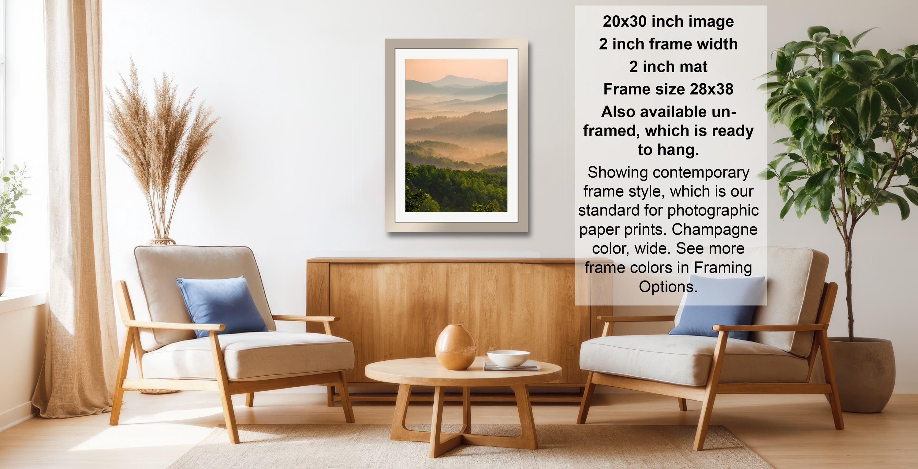 a living room with a framed landscape photograph hanging on the wall, a wooden coffee table in the center, and two armchairs facing each other.