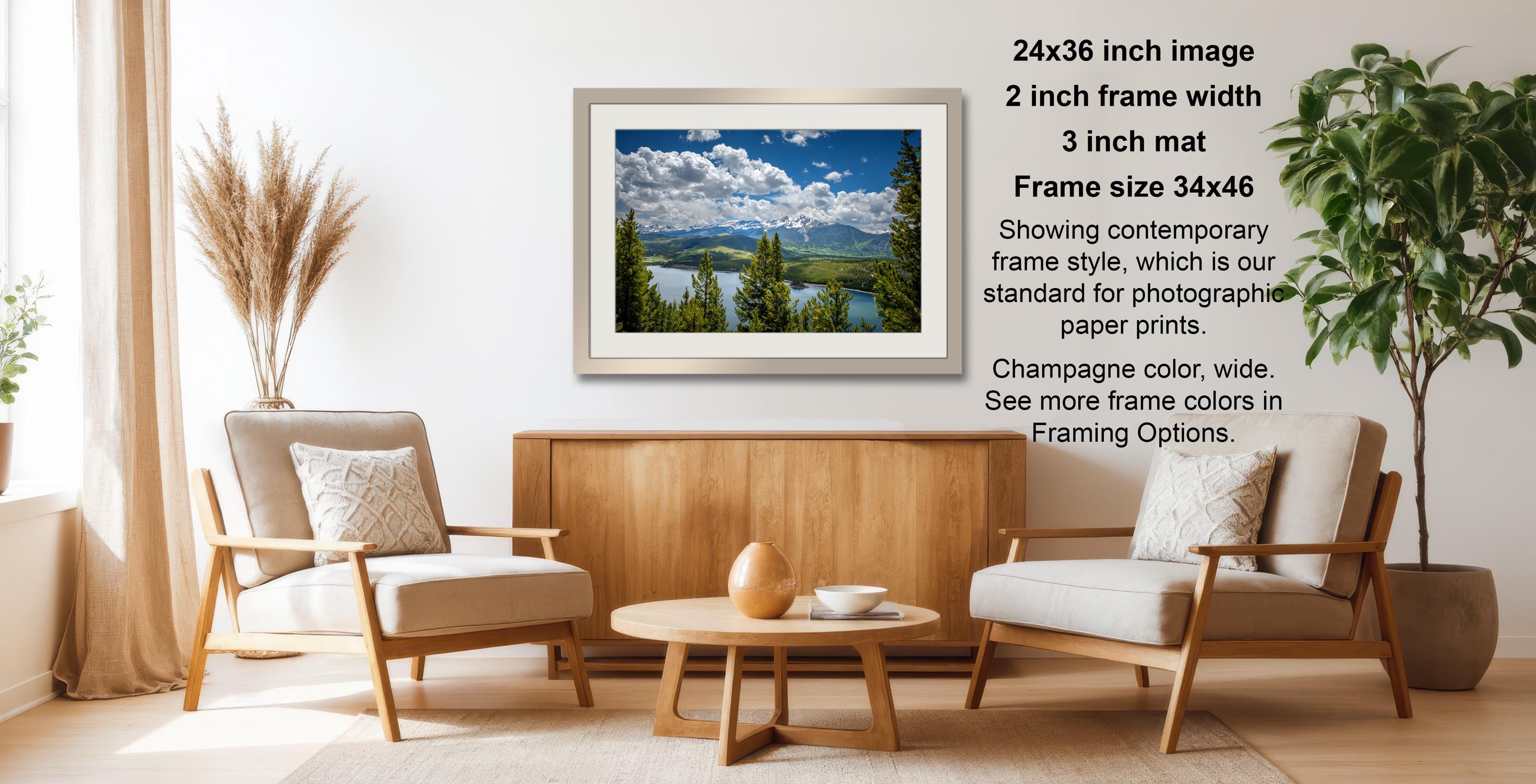 a cozy living room with a wooden coffee table, two beige armchairs, and a framed landscape photograph hanging on the wall.