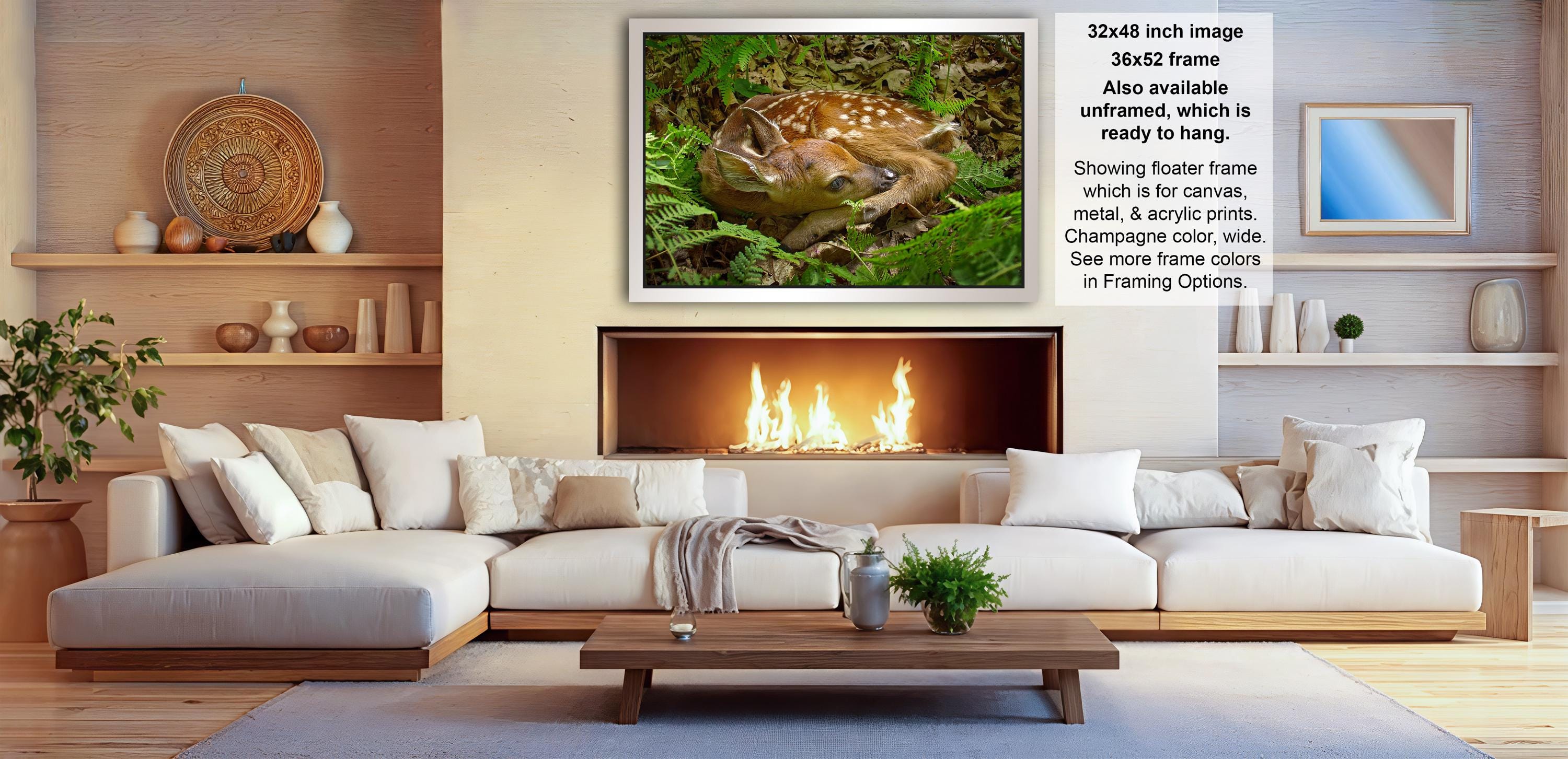 a cozy living room with a large white sofa, a fireplace, and a framed photograph of a deer resting in the forest.
