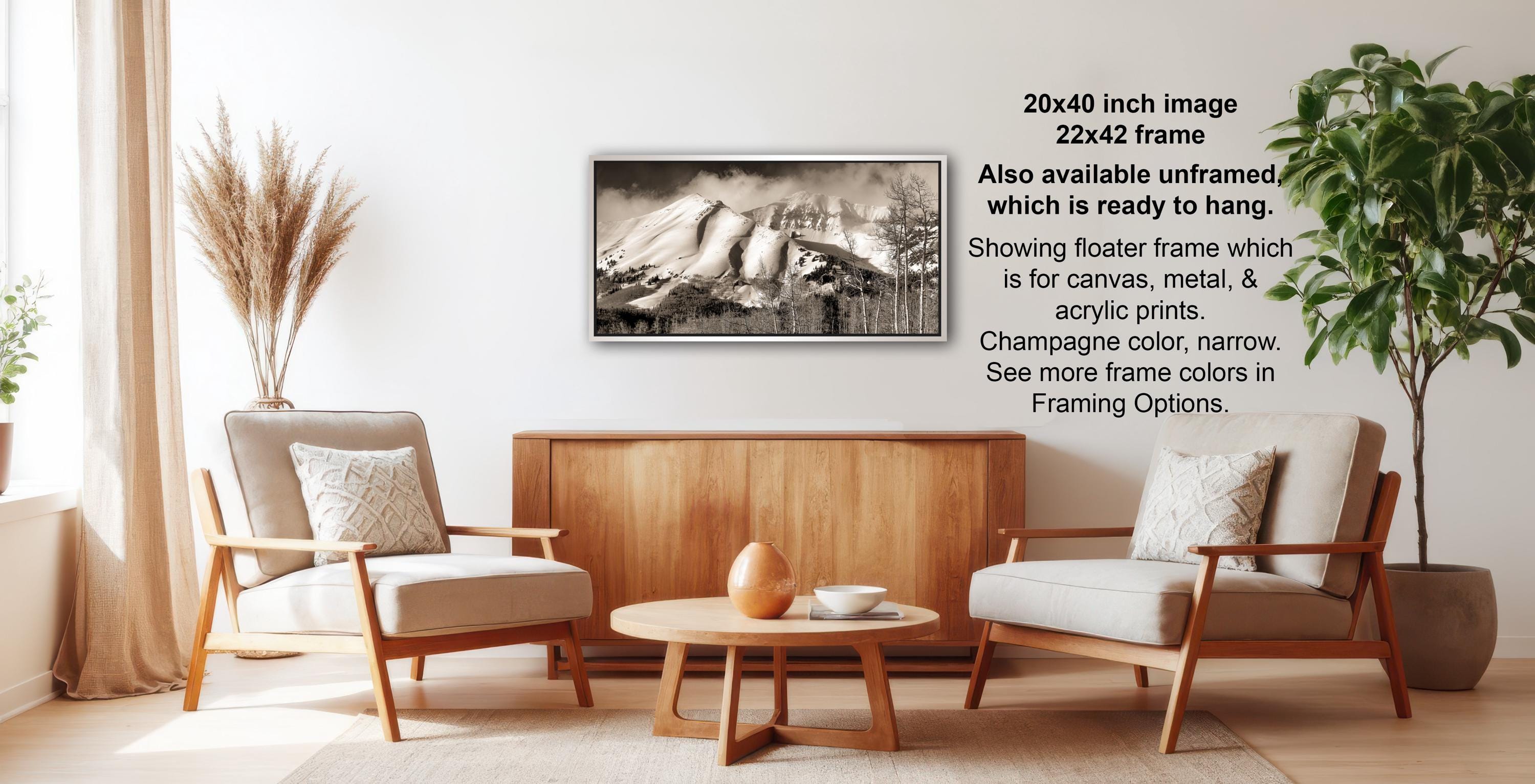 a living room with a wooden coffee table, two white armchairs, and a framed black and white photograph of a mountain landscape hanging on the wall.