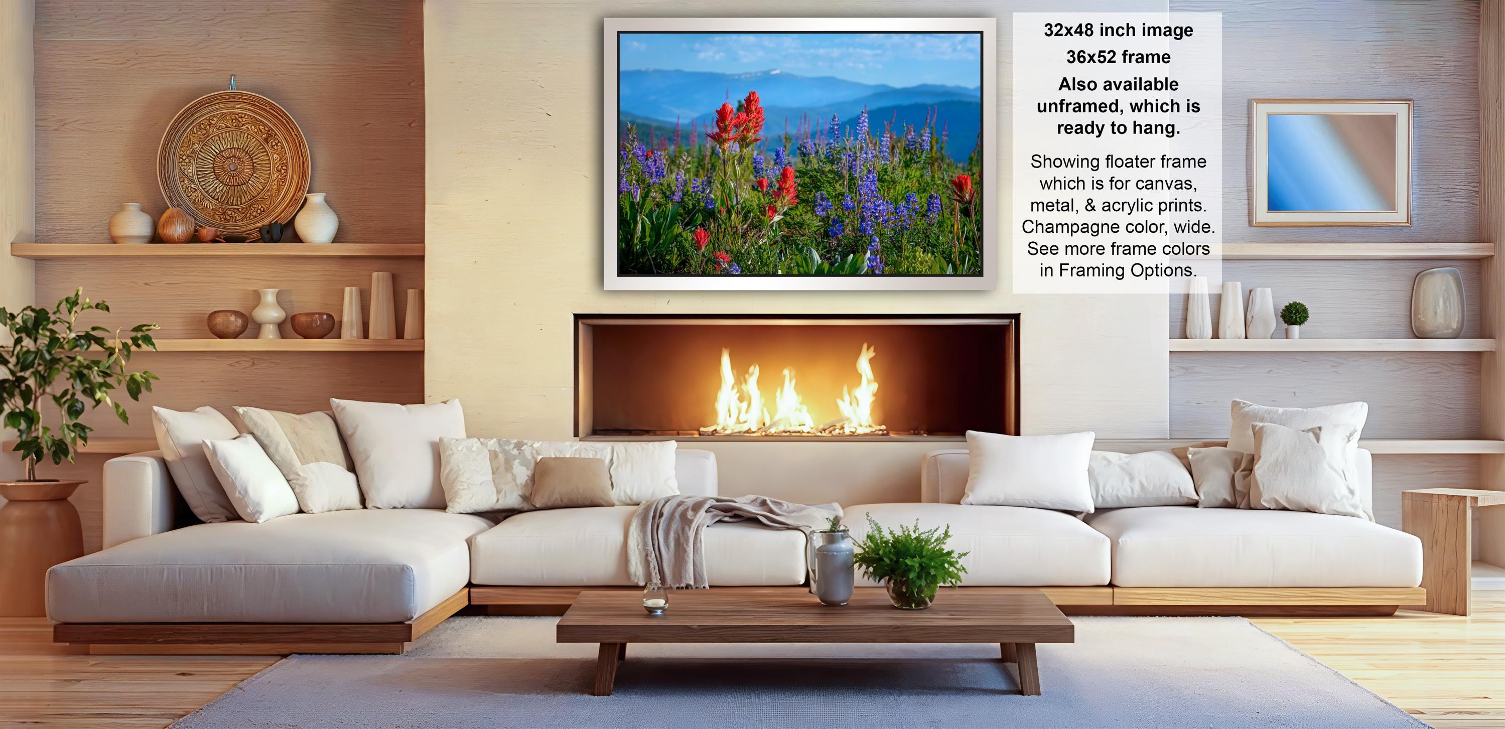 a cozy living room with a fireplace, white sofas, and a coffee table. The room has a warm and inviting atmosphere, with a large framed picture of a field of flowers hanging on the wall.