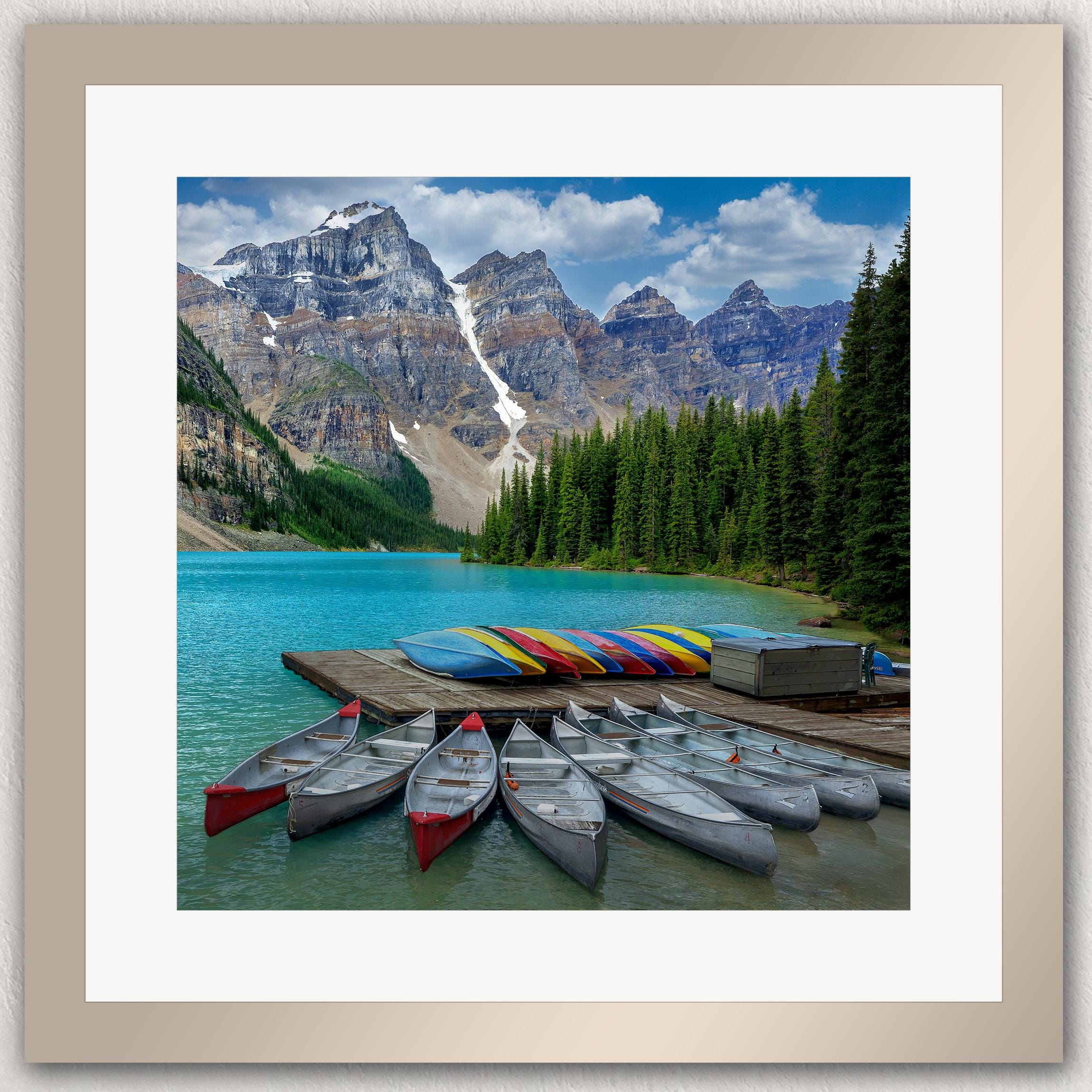 A scenic view of a lake surrounded by mountains, with a dock and colorful canoes lined up in the water.