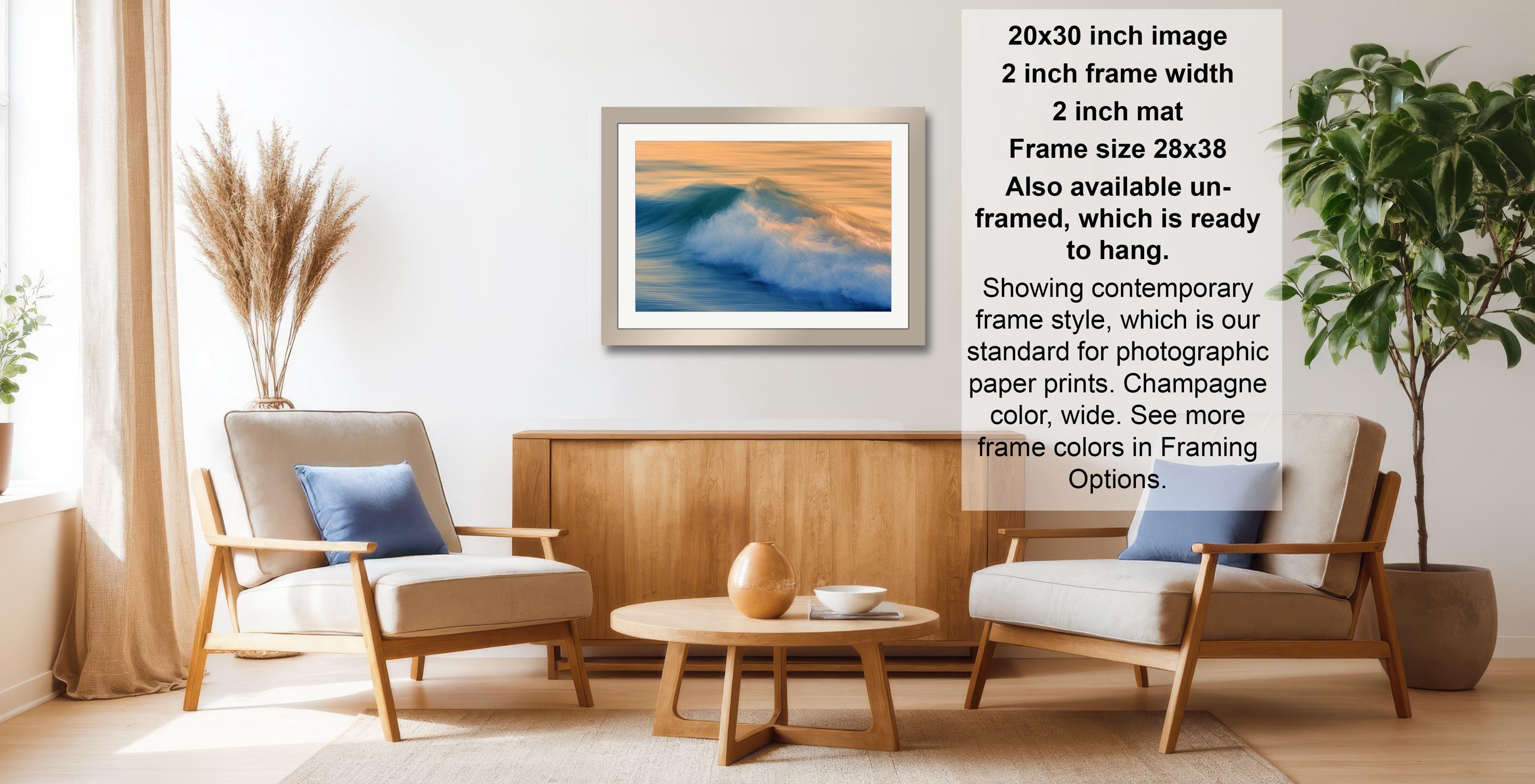 a living room with a wooden coffee table, two white armchairs, and a framed picture of a wave on the wall. The room has a modern and minimalist design, with a large window providing natural light.