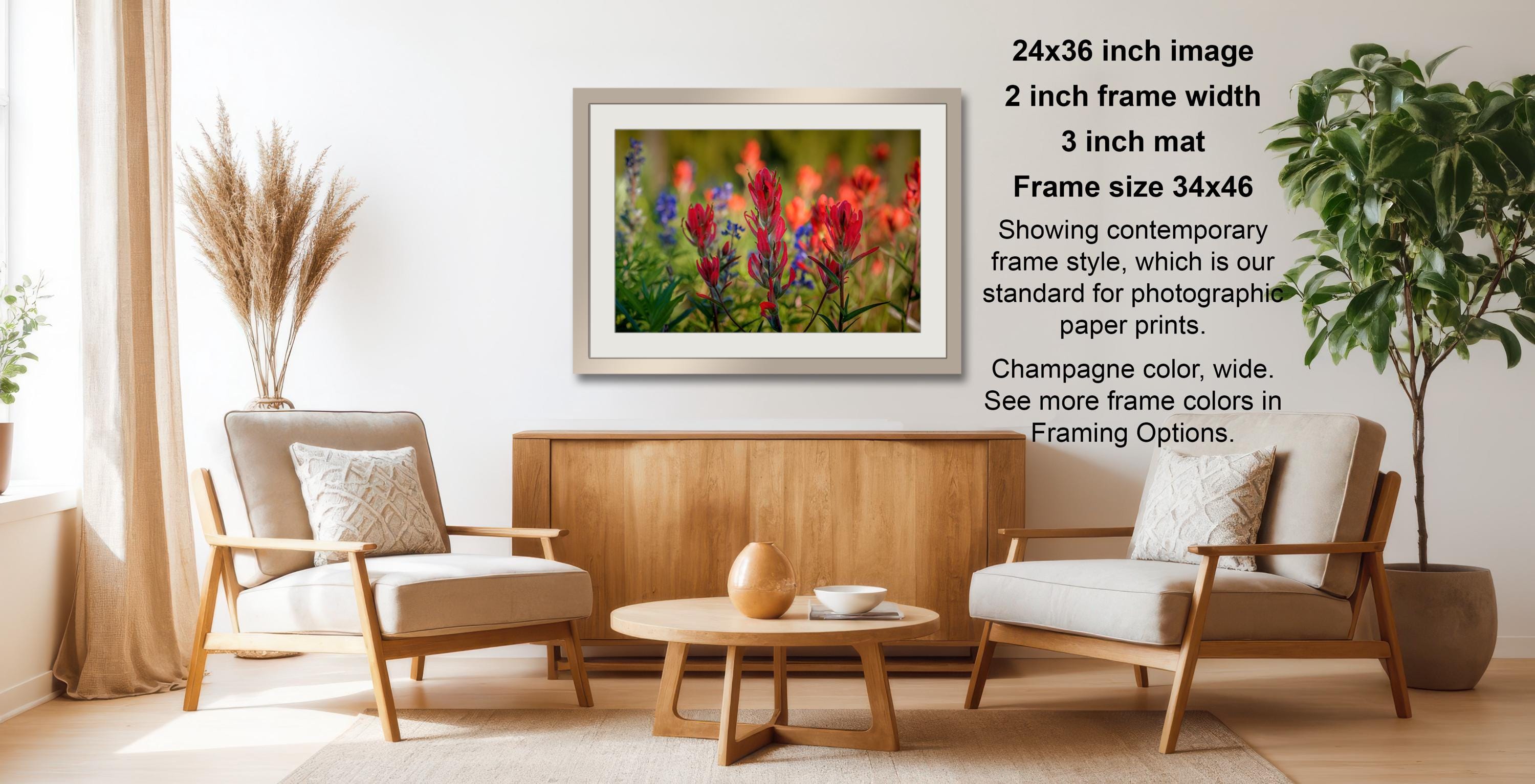 a living room with a wooden coffee table, two white armchairs, and a framed photograph of colorful flowers hanging on the wall.