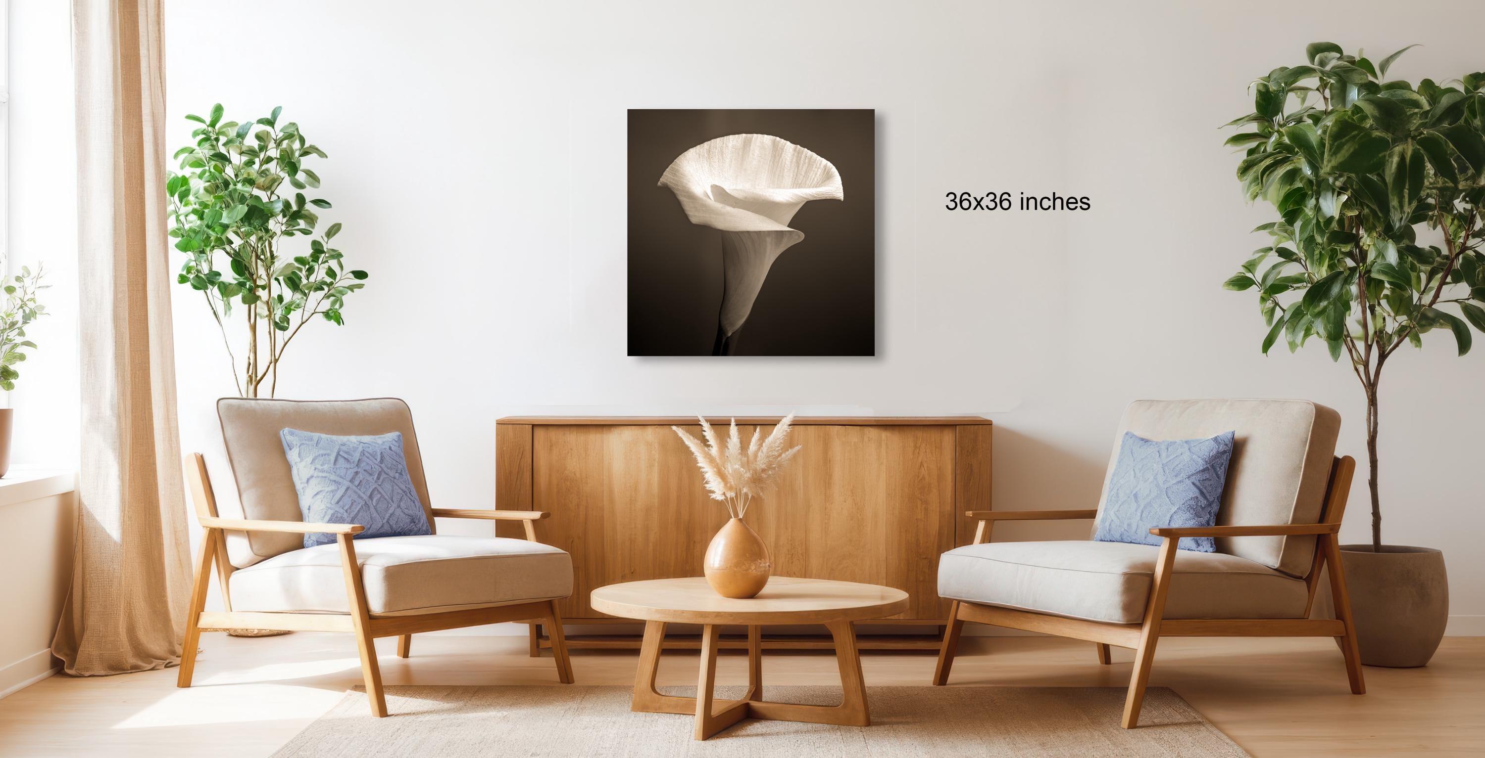 a living room with two beige armchairs, a wooden coffee table, and a large potted plant. A framed artwork of a white flower is hanging on the wall above the coffee table.