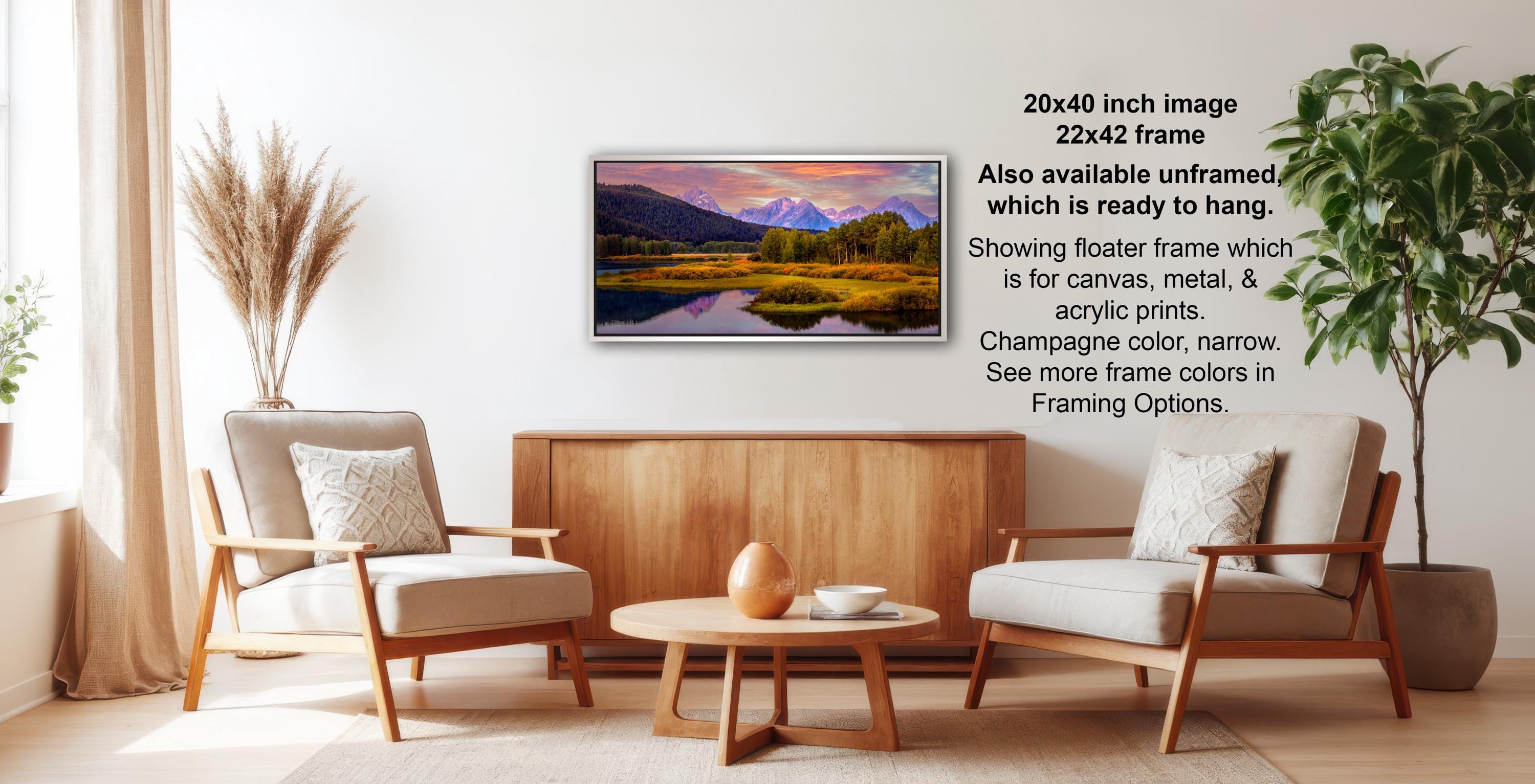 a living room with a wooden coffee table, two white armchairs, and a potted plant. A framed landscape painting is hanging on the wall above the coffee table.