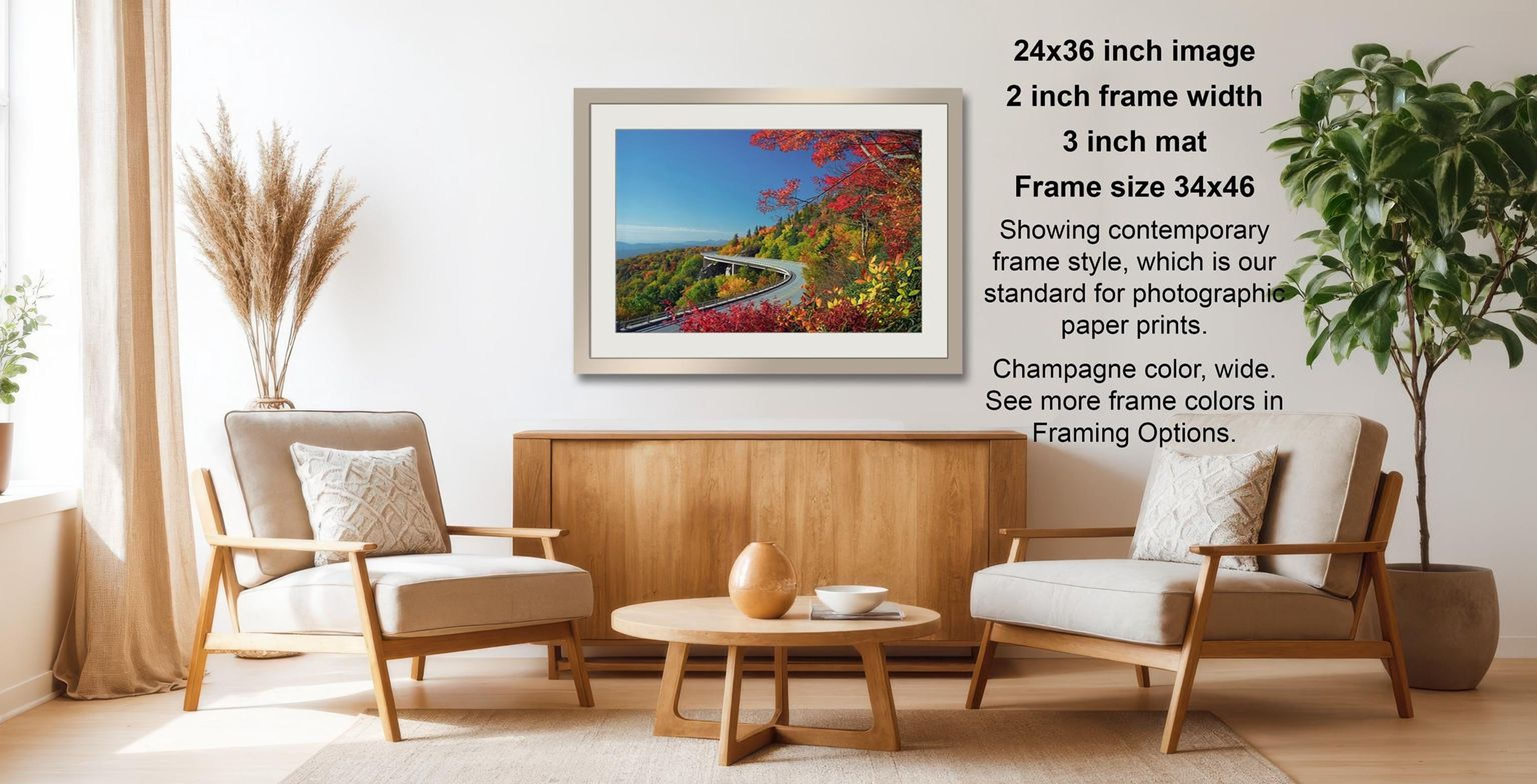 a living room with a framed landscape photograph hanging on the wall. The photograph is of a scenic mountain view with a winding road and colorful foliage. The room is furnished with two beige armchairs and a wooden coffee table, creating a cozy and inviting atmosphere.