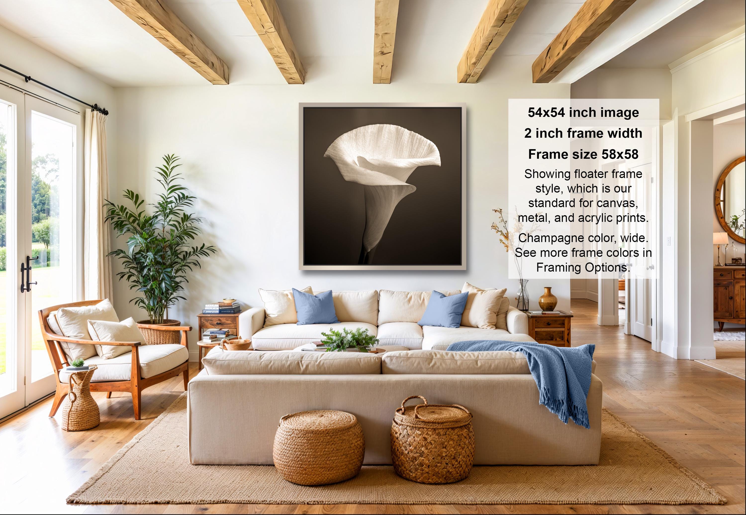 A modern living room with a large framed photograph of a white flower on the wall, a beige sofa, a wooden coffee table, and a potted plant.