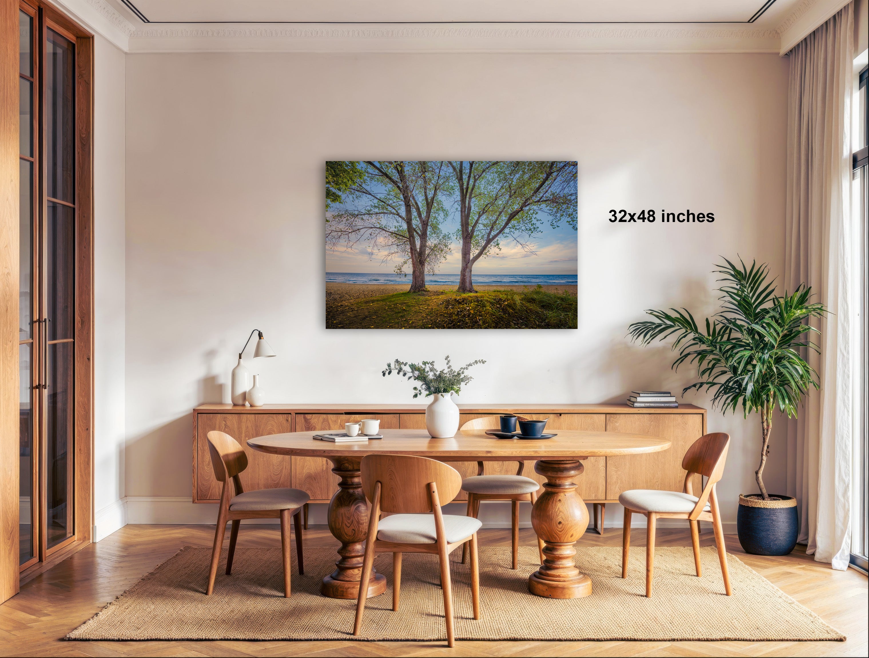 a serene dining room with a large wooden table surrounded by matching chairs. A painting of a tree-filled landscape is displayed on the wall above the table, adding a natural element to the room. The table is set with a vase of flowers and a potted plant, creating a cozy and inviting atmosphere.