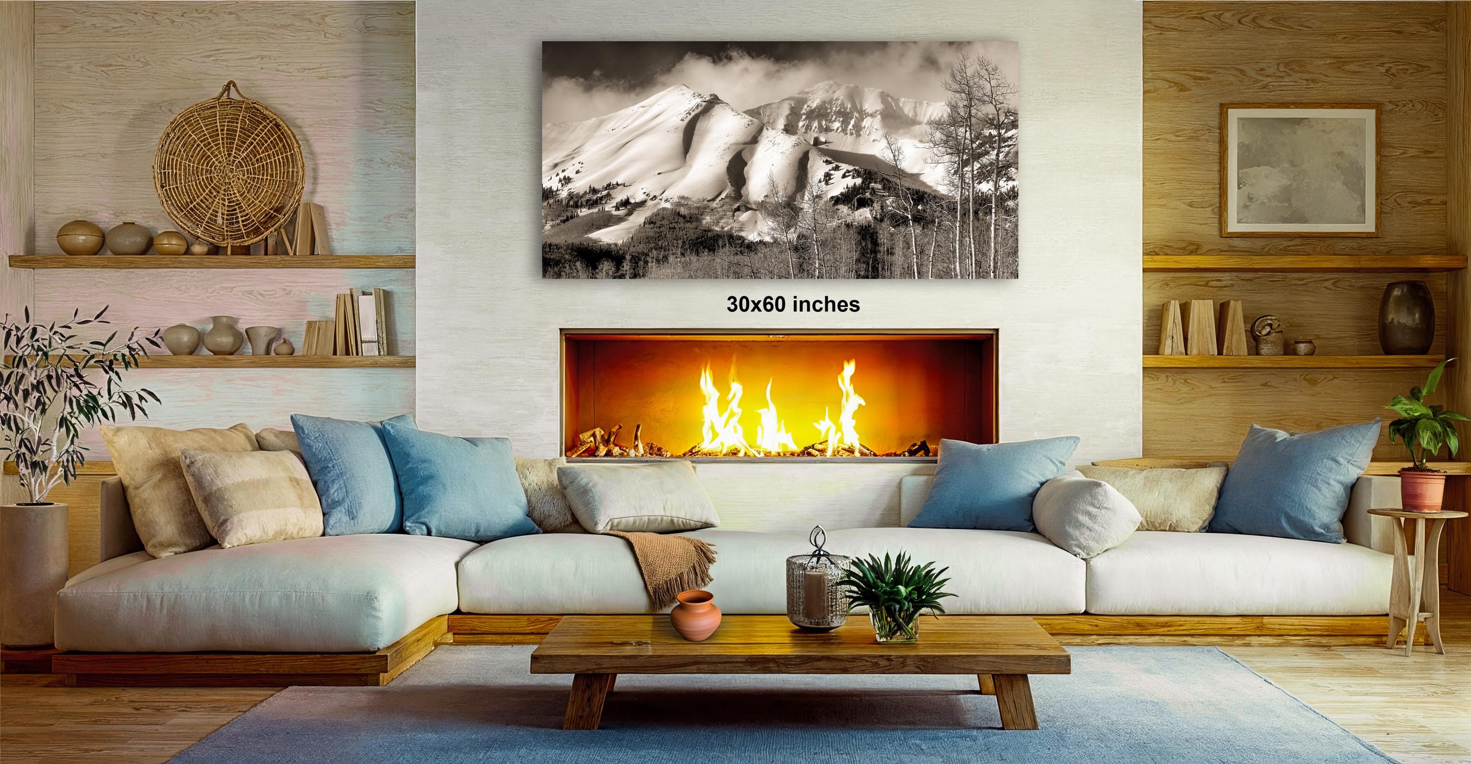 a cozy living room with a fireplace, a large framed black and white photograph of a snowy mountain range, and a wooden coffee table in front of the fireplace.