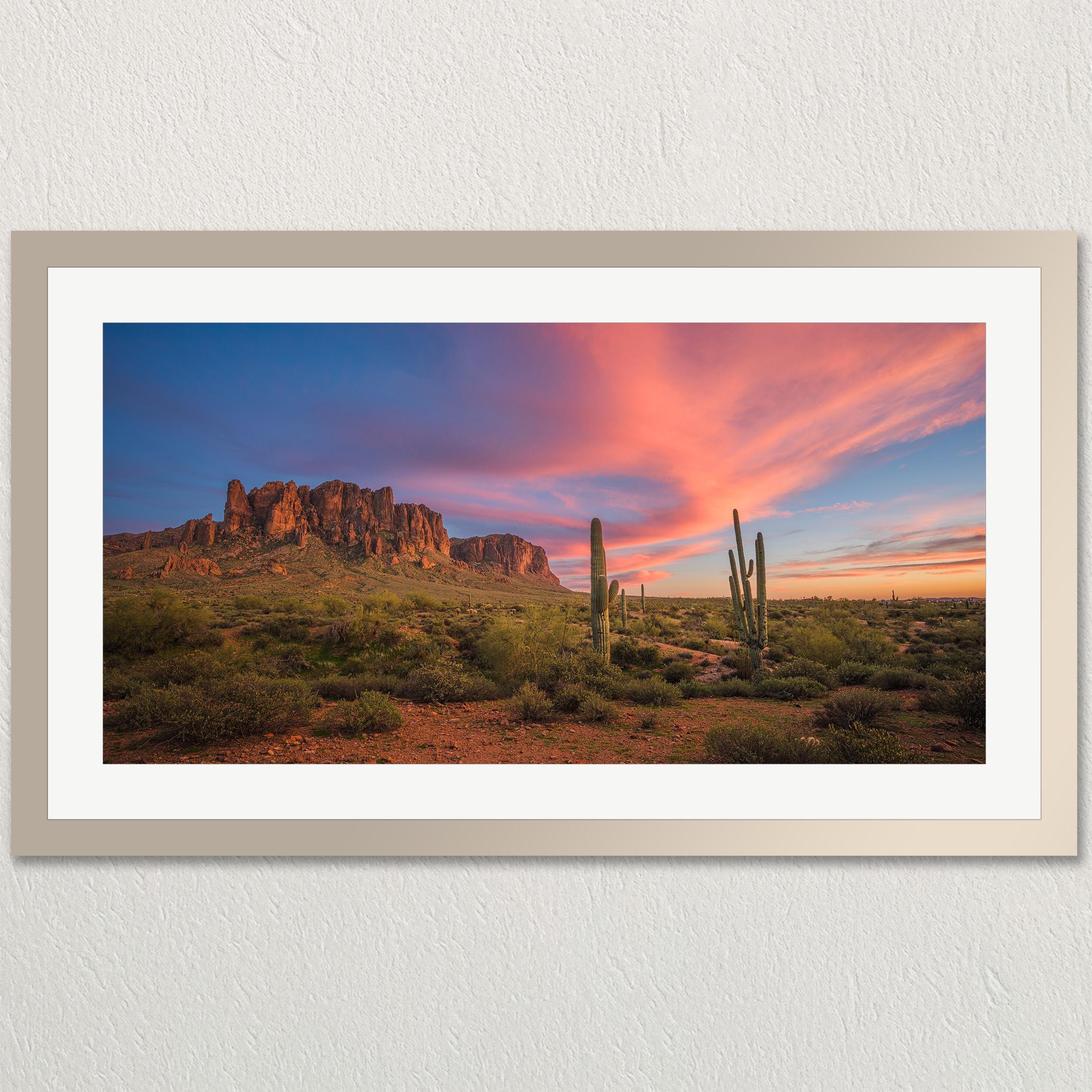 A framed photograph depicting a desert landscape at sunset, with a mountain range in the background and a colorful sky.