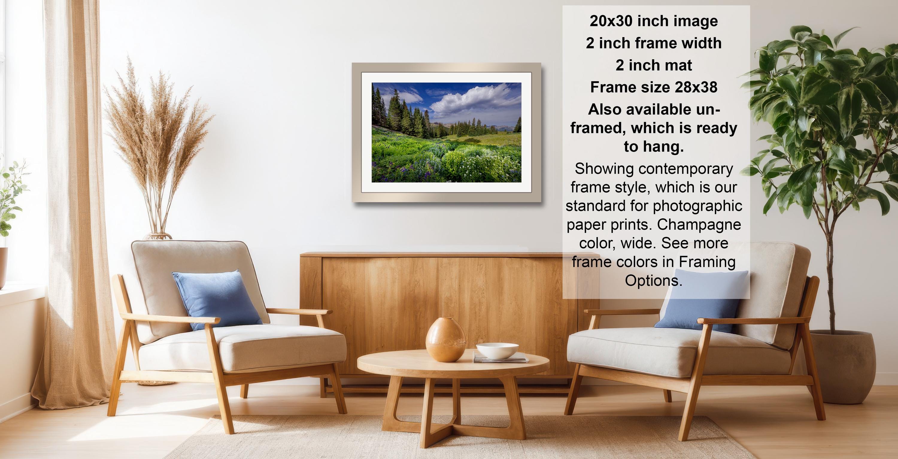 a living room with a framed landscape photograph hanging on the wall, a wooden coffee table in the center, and two armchairs facing each other.