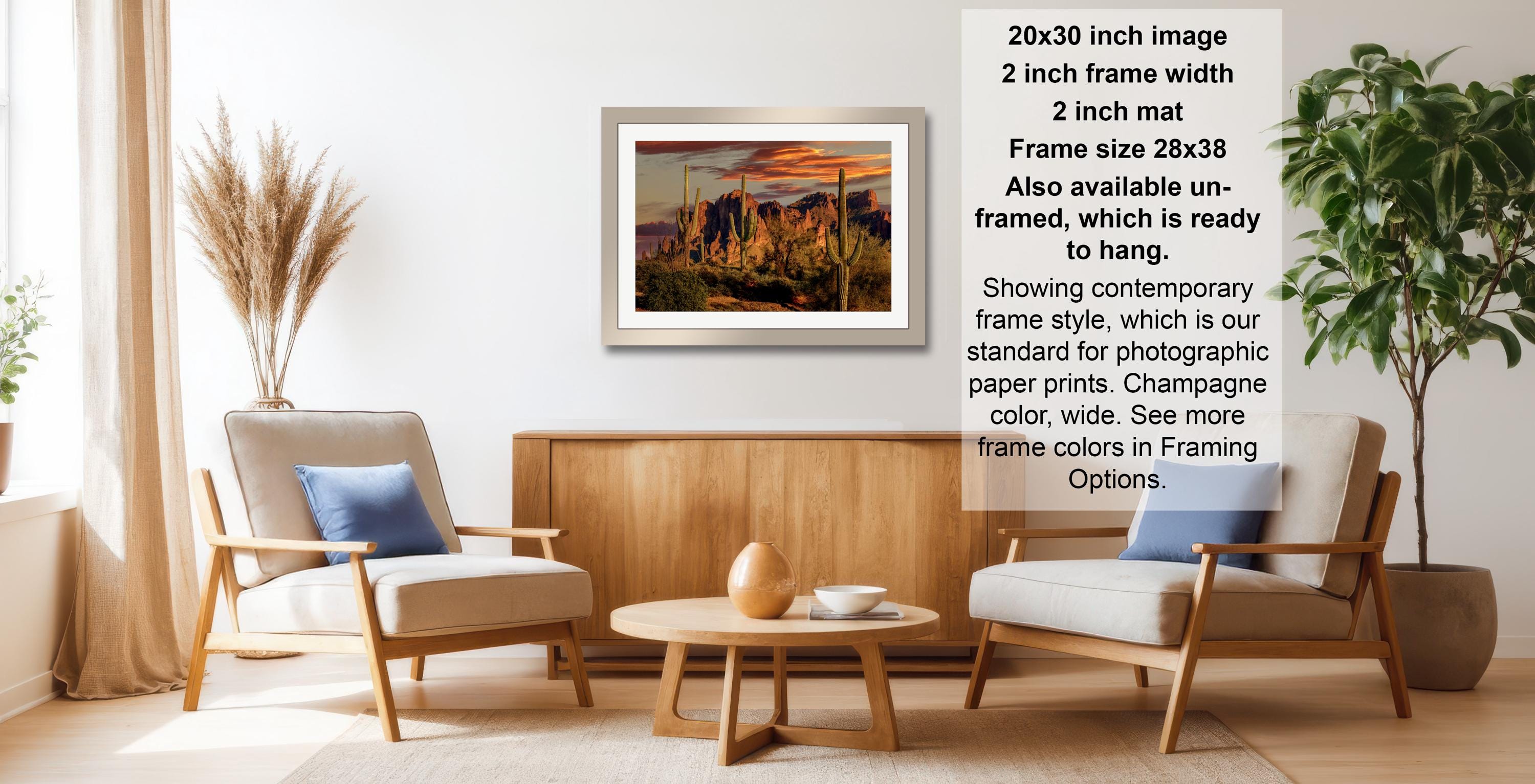 a living room with a framed landscape photograph hanging on the wall, a wooden coffee table in the center, and two chairs facing each other.