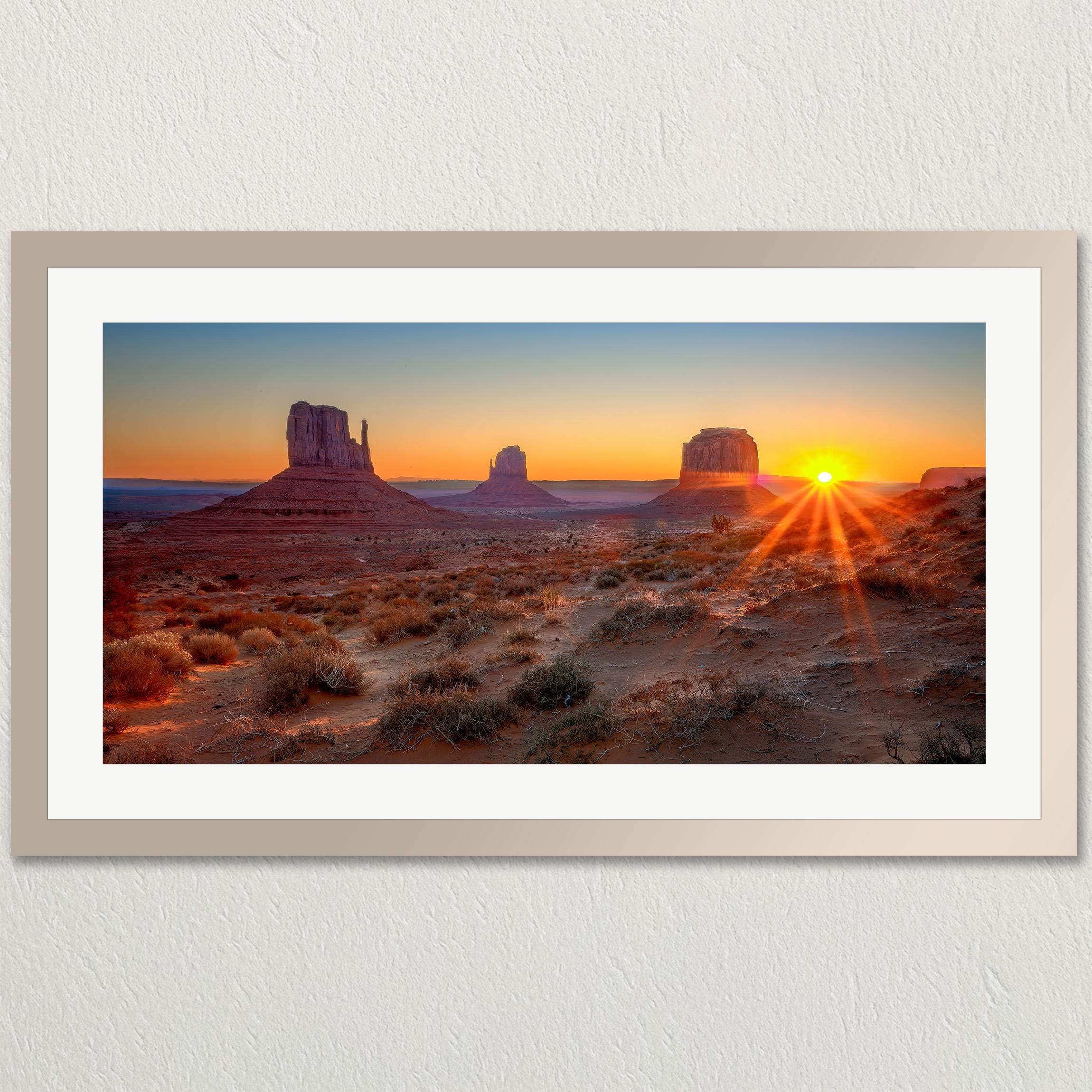 A framed photograph depicting the iconic rock formations of Monument Valley at sunset, with the sun's rays creating a dramatic effect on the landscape.