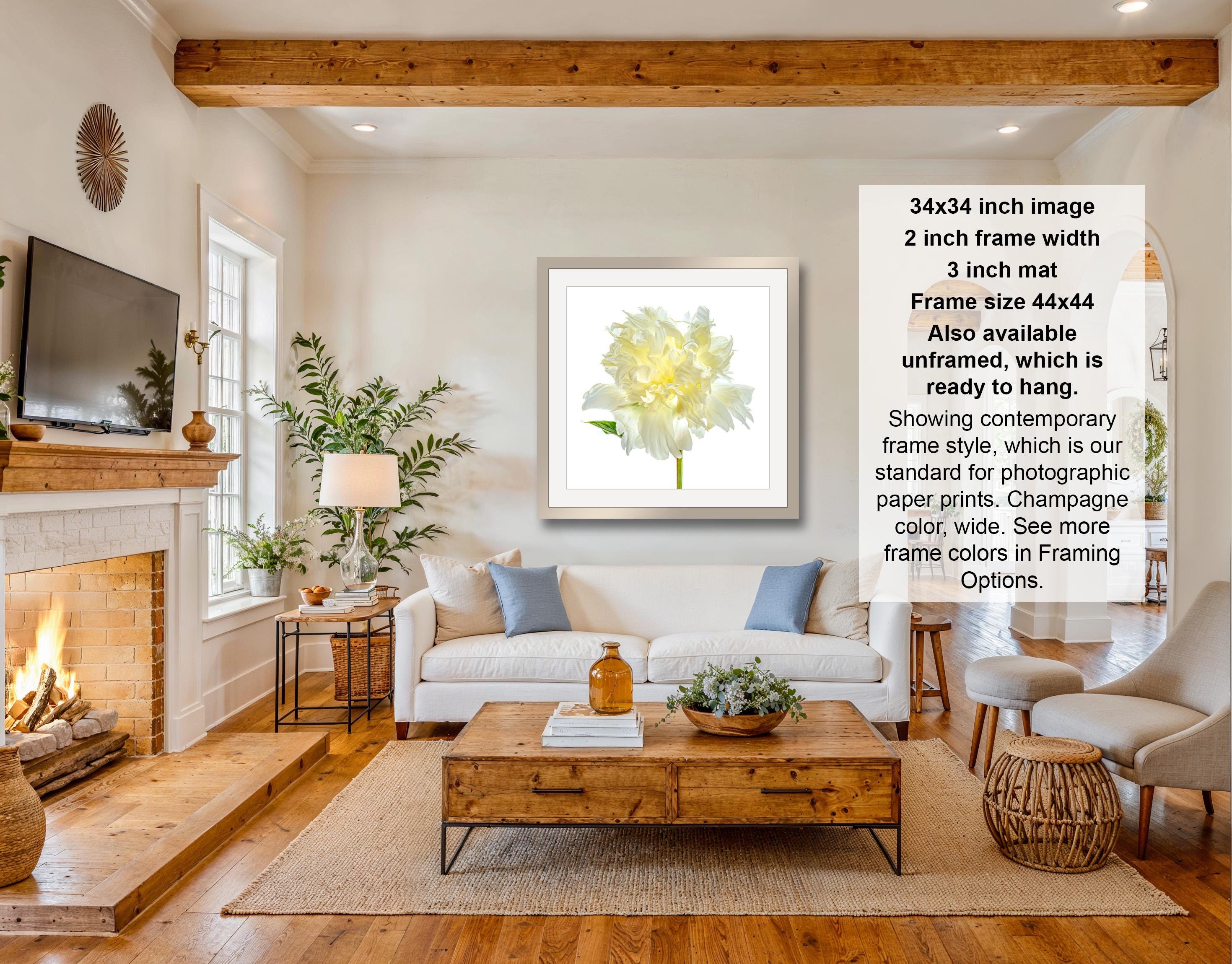 The image is a living room with a fireplace, a white sofa, a wooden coffee table, and a framed print of a yellow flower on the wall.