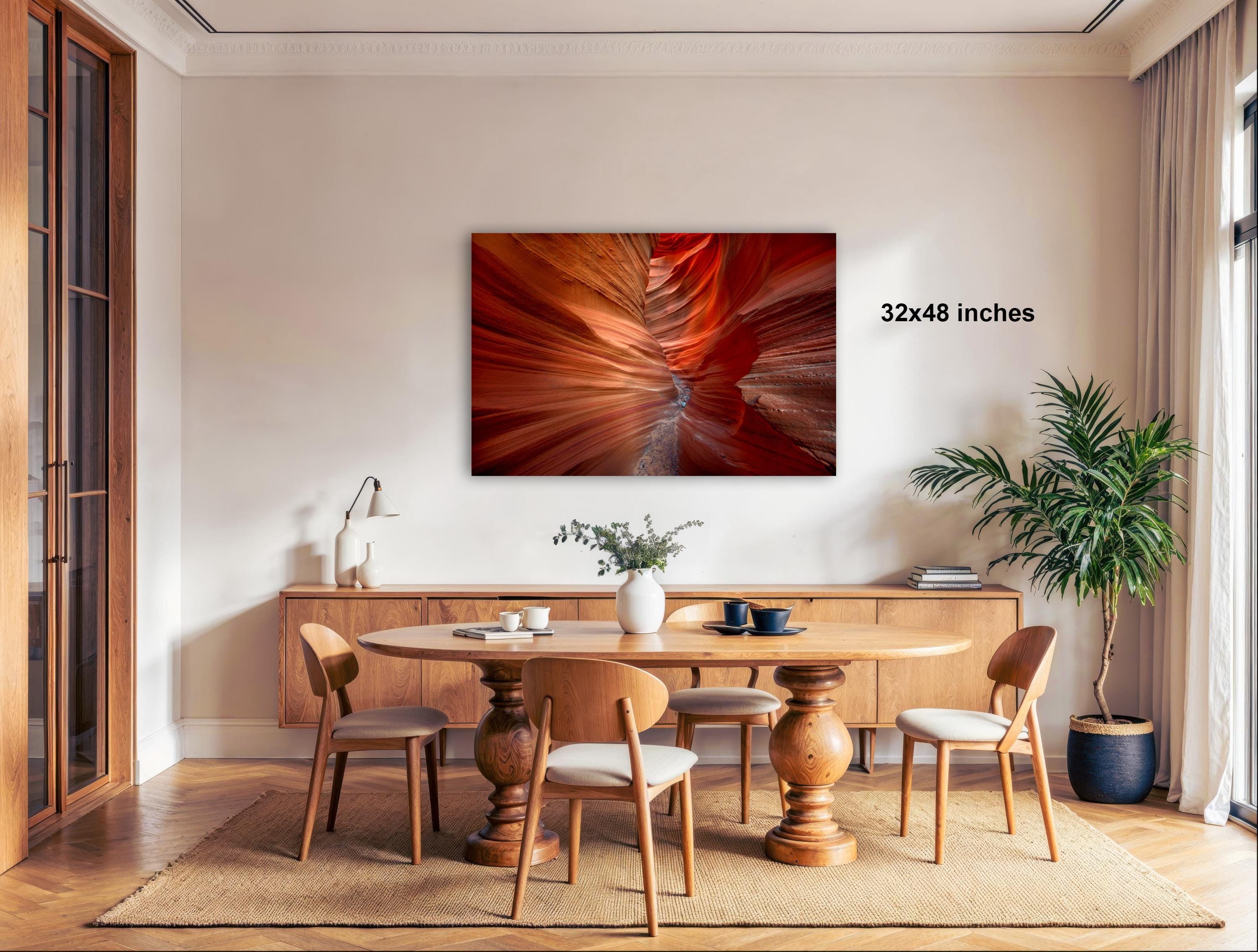 a modern dining room with a large wooden table surrounded by matching chairs. A large abstract painting with vibrant red and orange colors is displayed on the wall above the table. The room is decorated with various plants and other furnishings, creating a warm and inviting atmosphere.