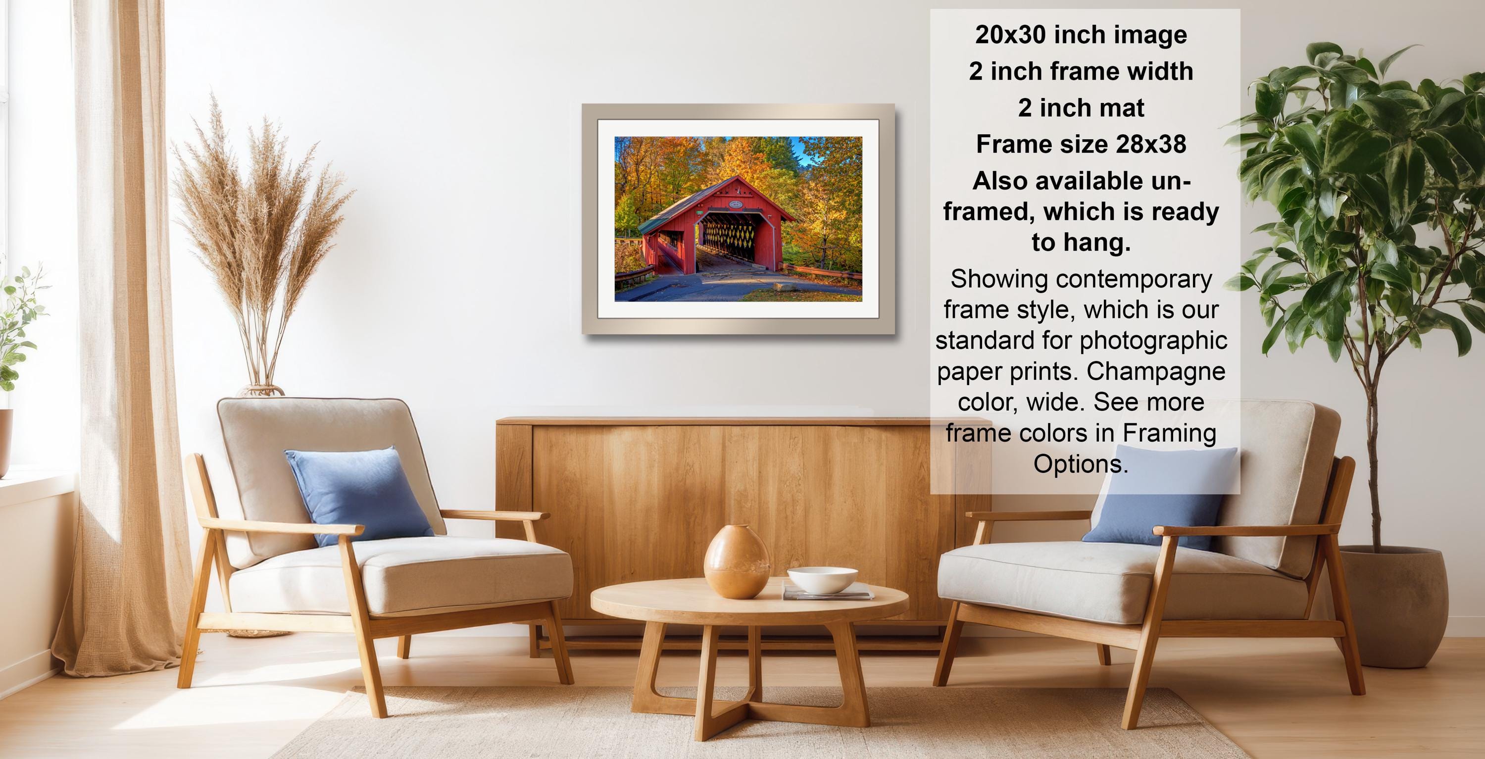 a cozy living room with a wooden coffee table, two beige armchairs, and a framed picture of a red bridge. The room is decorated with potted plants and a vase, creating a warm and inviting atmosphere.