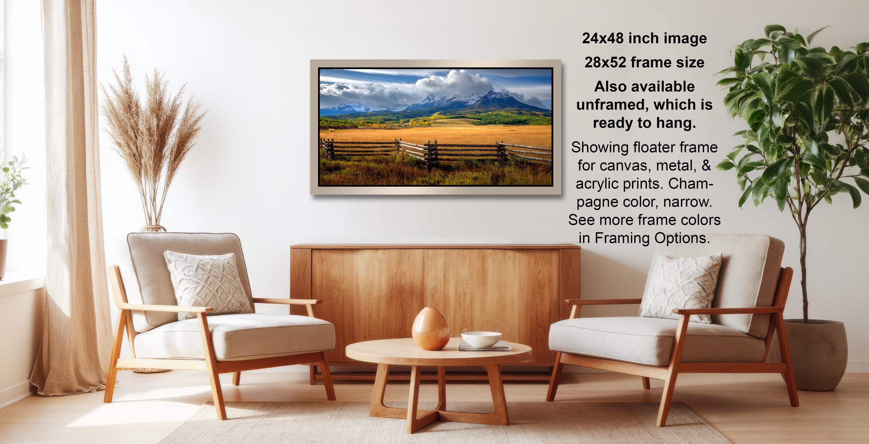 a living room with a wooden coffee table, two white armchairs, and a framed landscape photograph hanging on the wall.