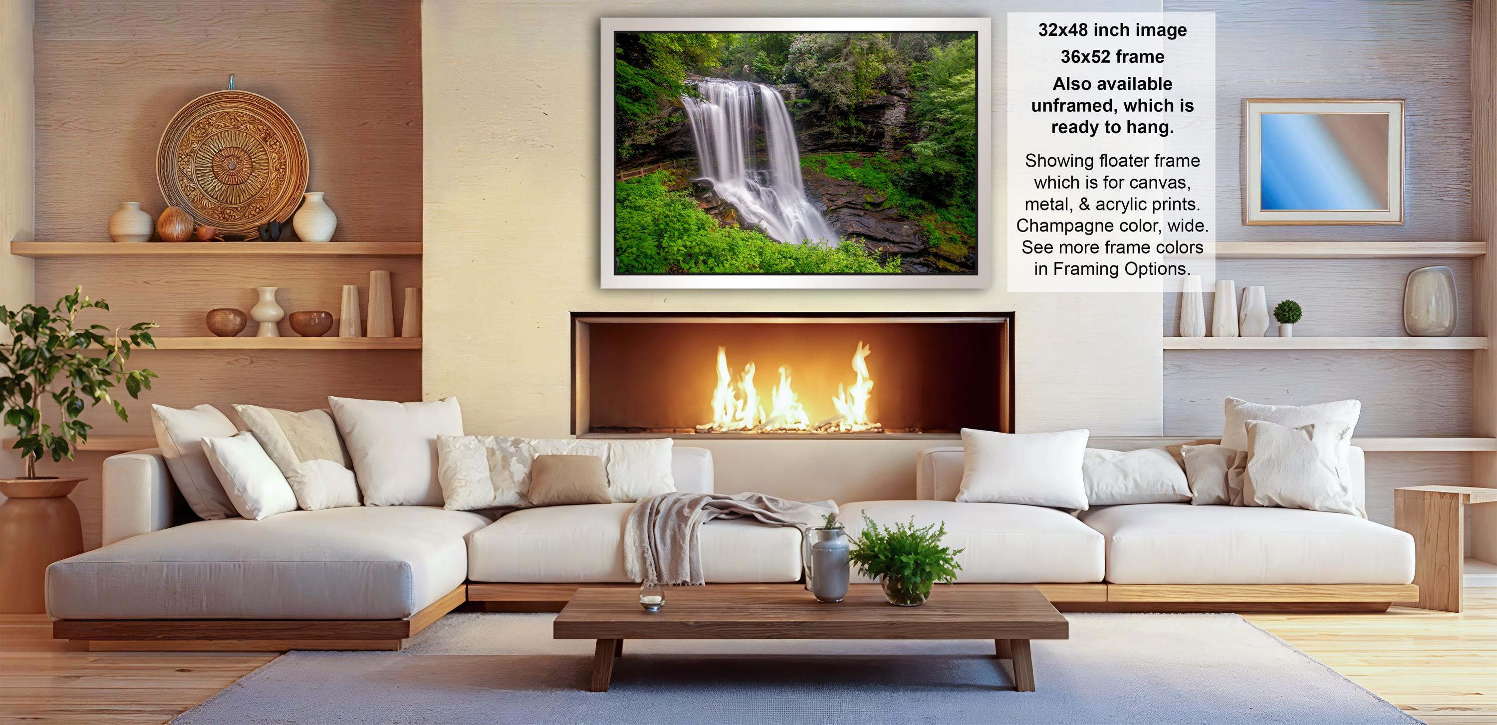 a cozy living room with a fireplace, white sofas, and a coffee table. The room has a warm and inviting atmosphere, with a fireplace providing a focal point and a painting of a waterfall adding an artistic touch.