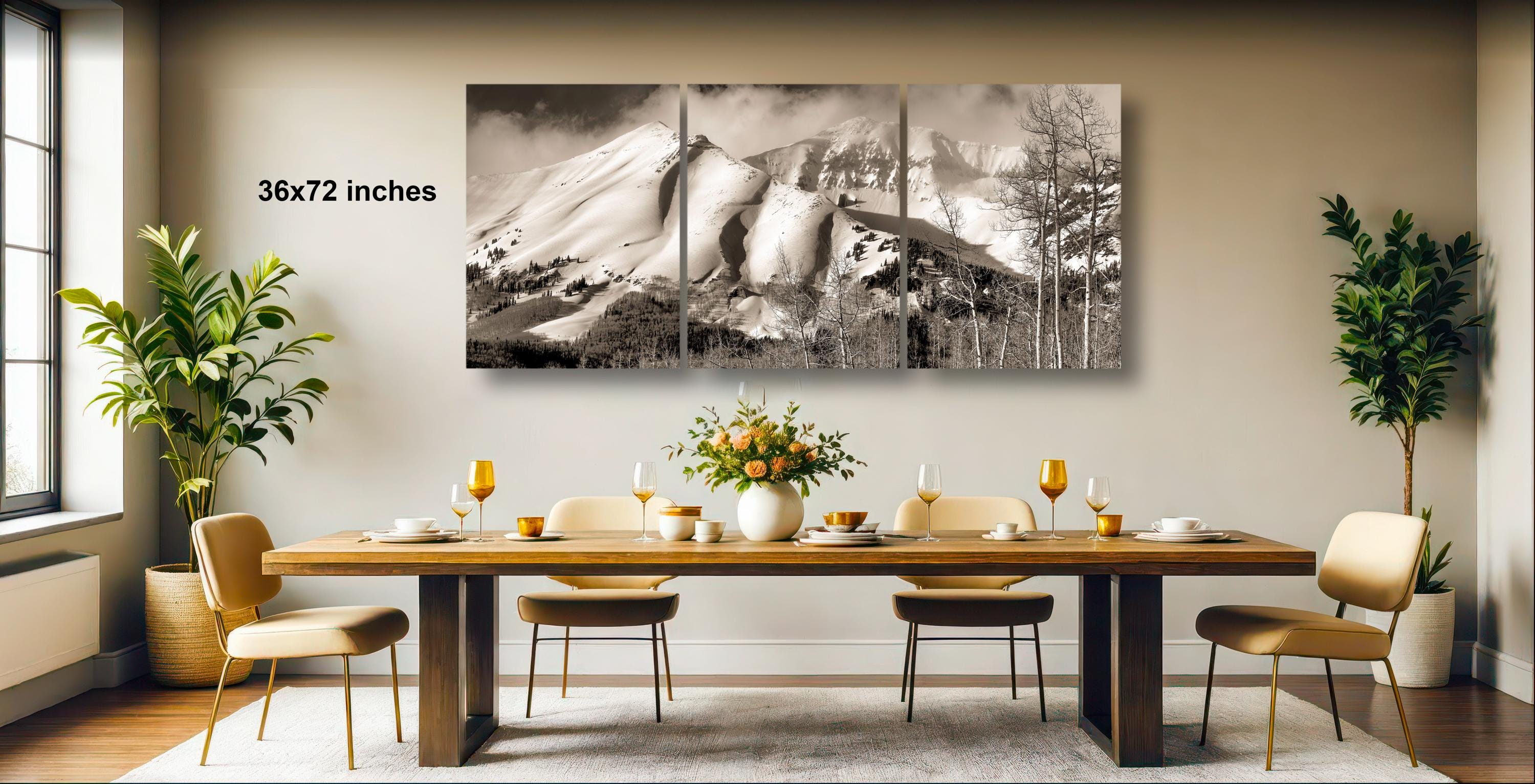 a large black and white photograph of a mountain landscape, which is hanging on the wall above a wooden dining table set with wine glasses, plates, and a vase of flowers.