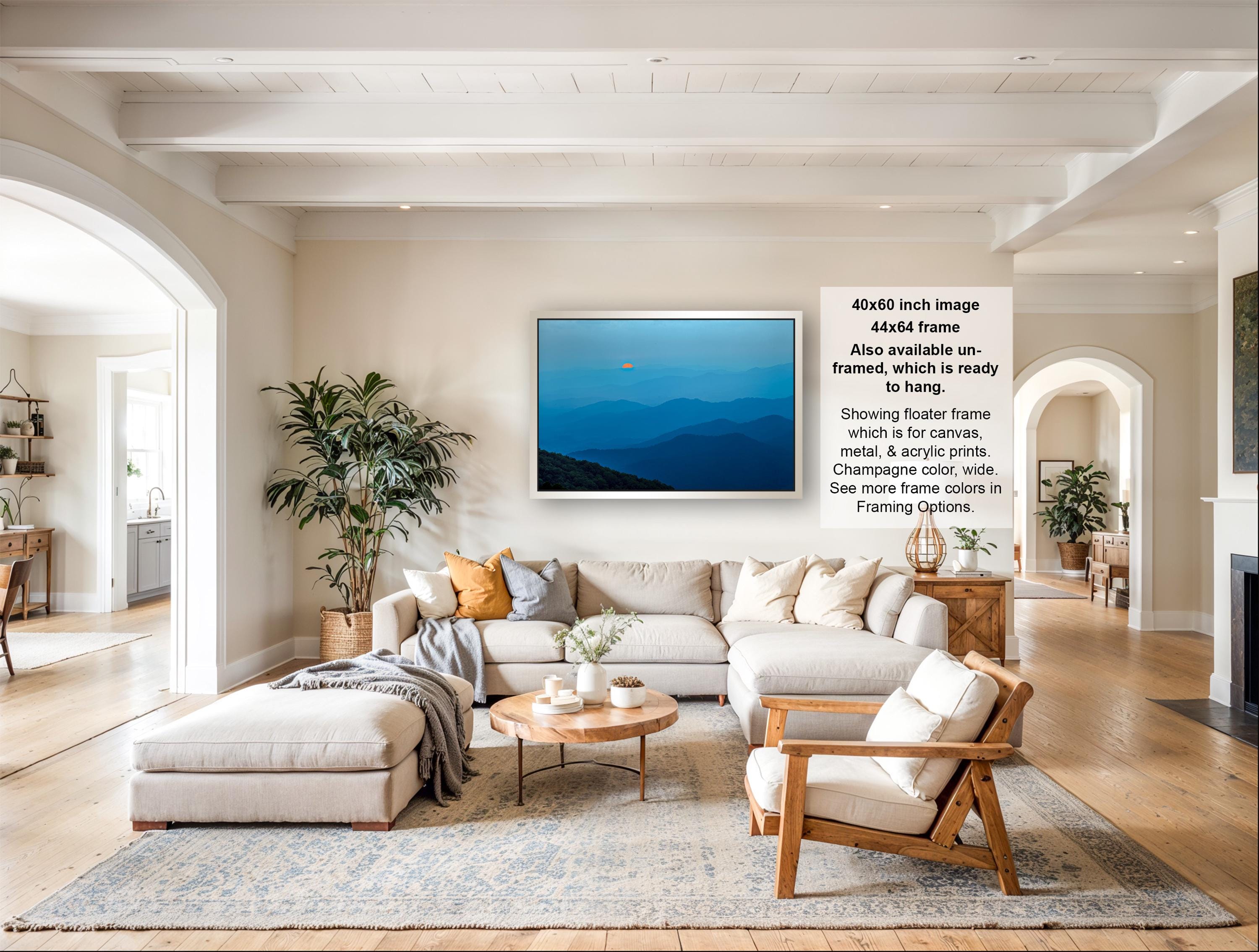 The image is a spacious living room with a large sectional sofa, a coffee table, and a fireplace. The room is decorated with various plants and has a neutral color scheme.