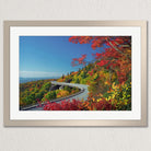 A framed photograph depicting a winding road surrounded by a vibrant autumn landscape, with colorful foliage and a clear blue sky.