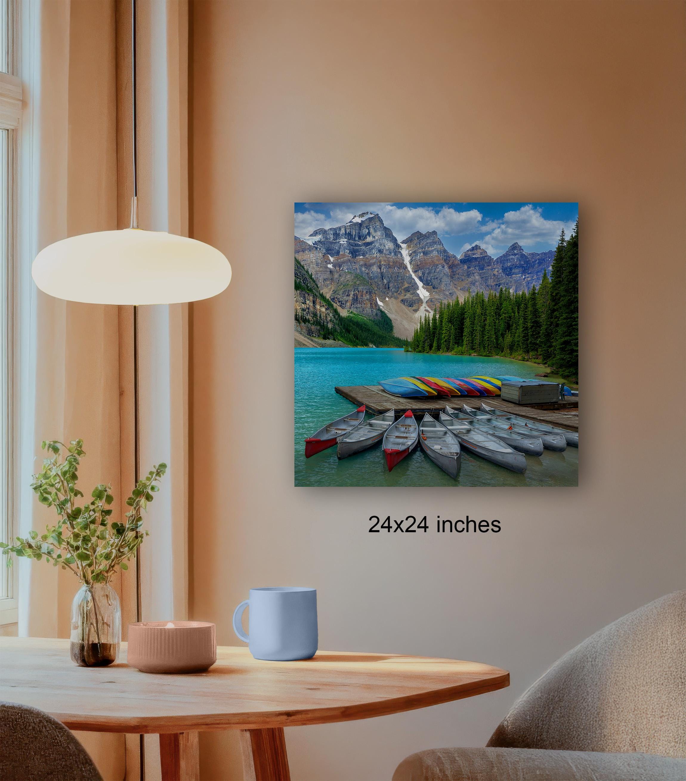 a wooden dining table with a blue mug, a candle, and a plant, set against a wall with a framed photograph of a mountain lake and colorful boats docked at a pier.