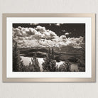 A black and white landscape photograph depicting a mountainous area with a lake or river in the foreground, surrounded by trees.