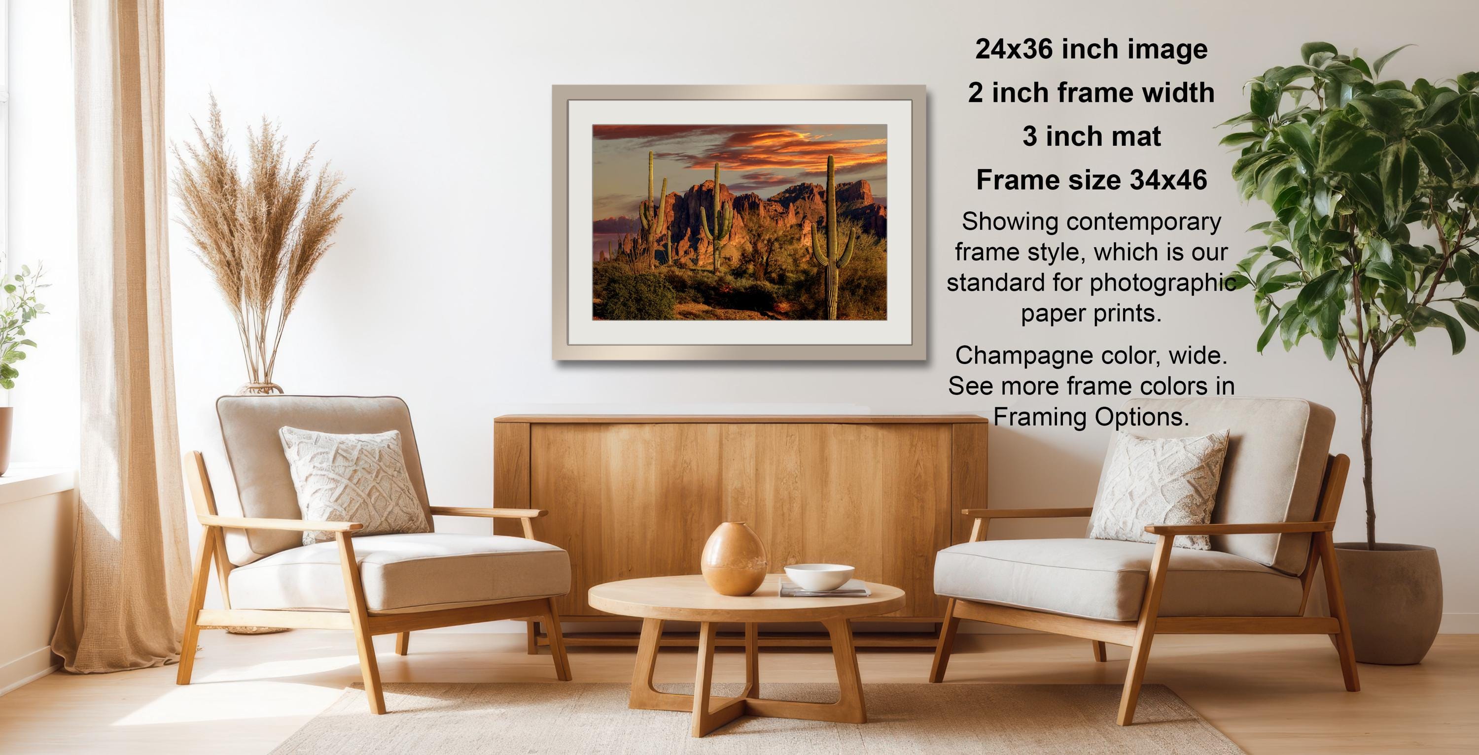 a living room with a wooden coffee table, two white armchairs, and a framed desert landscape photograph hanging on the wall.
