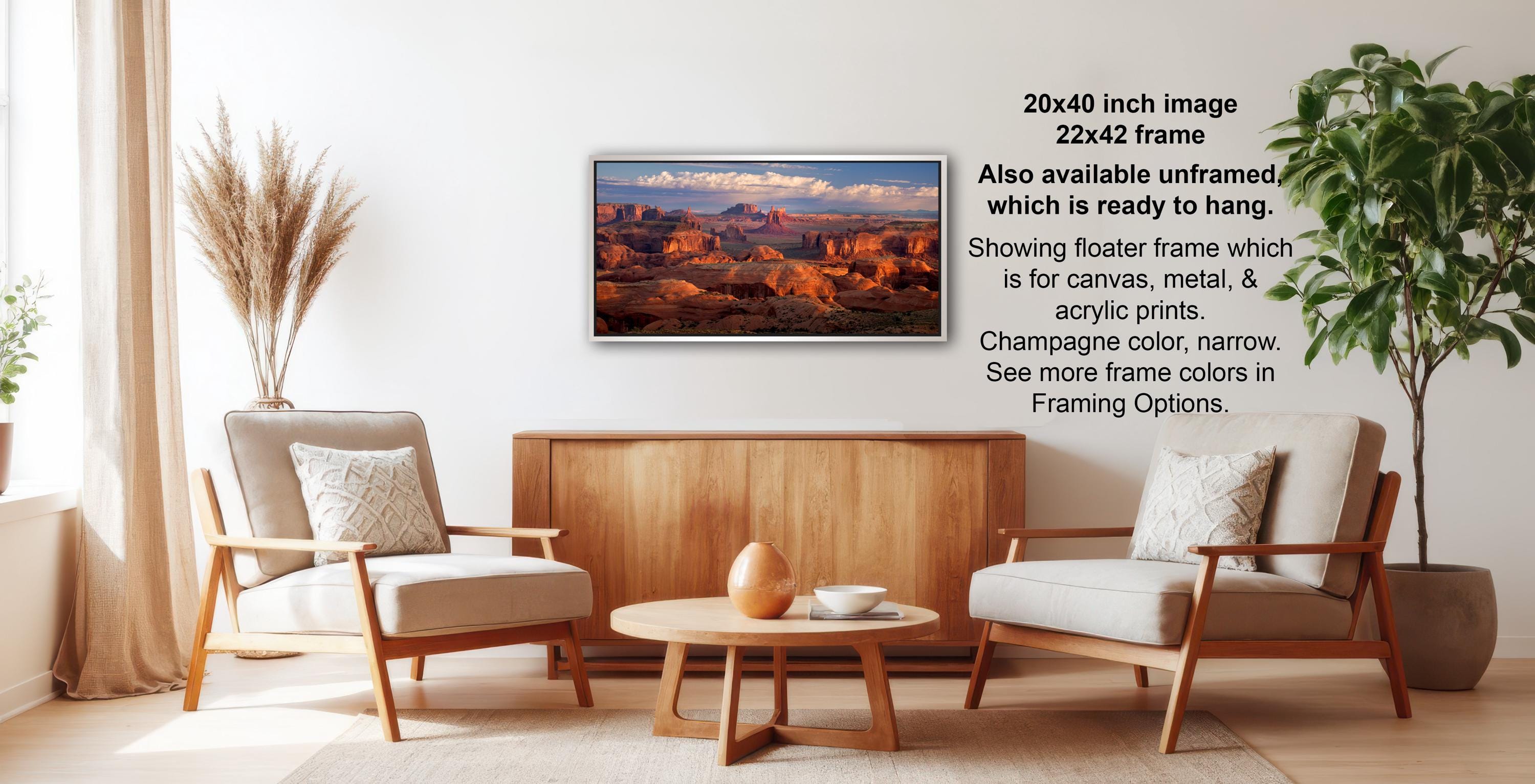a living room with a wooden coffee table, two white armchairs, and a framed landscape painting hanging on the wall.