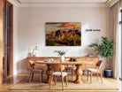 a dining room with a large wooden table surrounded by chairs, a potted plant, and a painting of a desert landscape hanging on the wall.