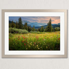 A framed photograph depicting a vibrant meadow filled with colorful wildflowers, surrounded by a forest and mountains in the distance.