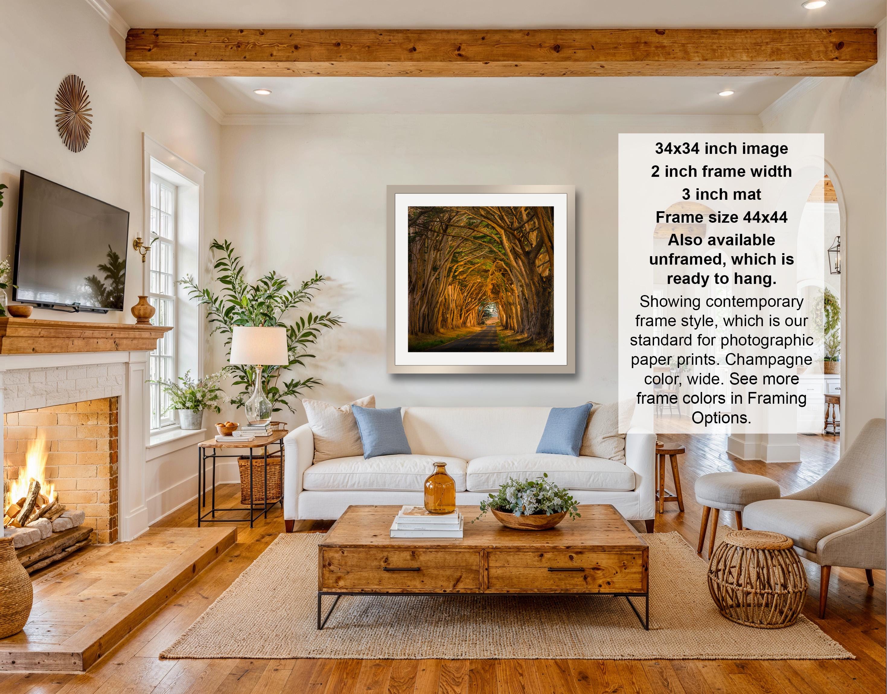 The image is a living room with a fireplace, a white sofa, a wooden coffee table, and a framed artwork hanging on the wall. The artwork depicts a tunnel with a light at the end. The room has a warm and cozy atmosphere, with a fireplace and various decorative elements such as potted plants and vases.
