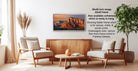 a living room with a wooden coffee table, two white armchairs, and a potted plant. Above the coffee table, there is a framed landscape photograph of a mountain range.