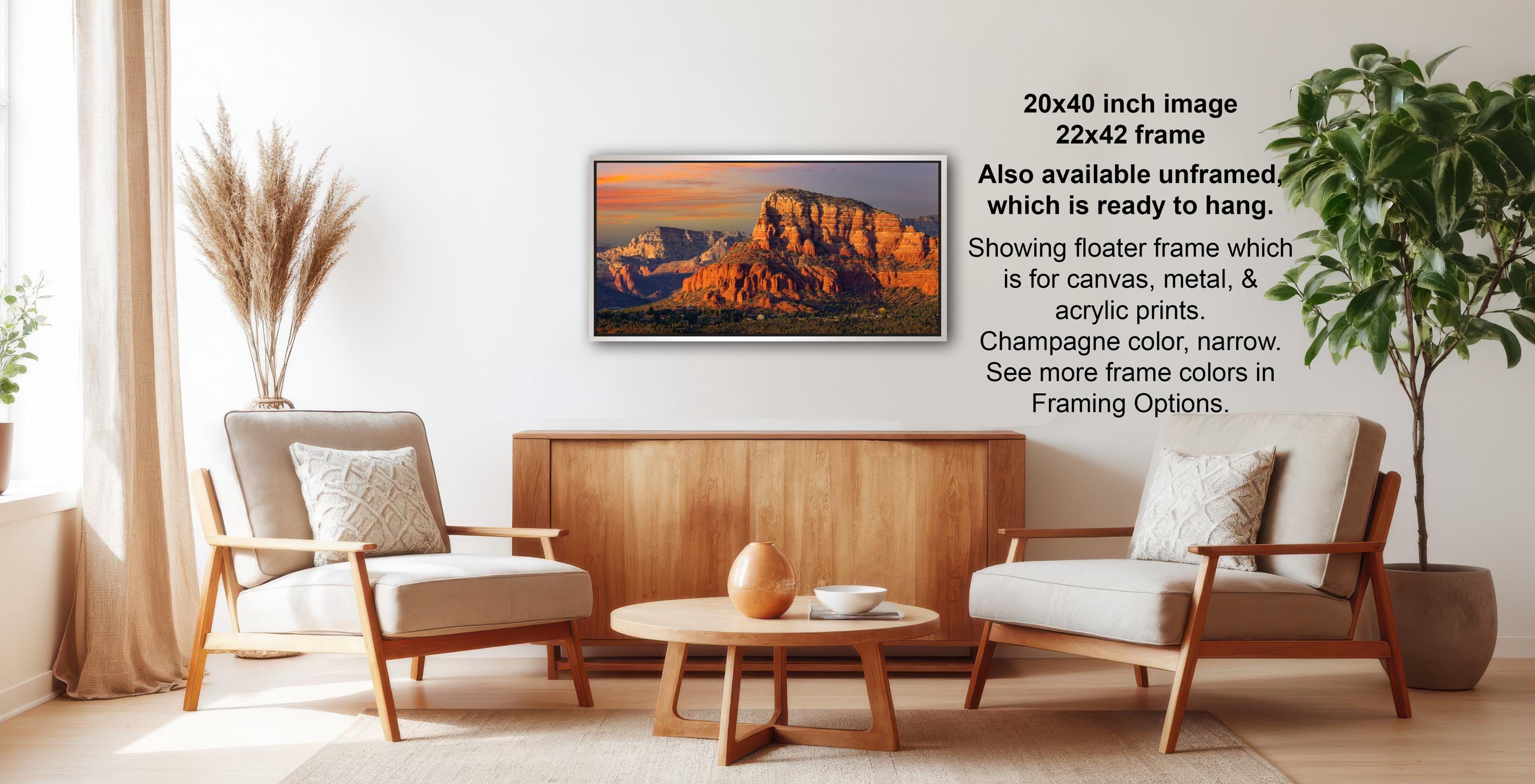 a living room with a wooden coffee table, two white armchairs, and a potted plant. Above the coffee table, there is a framed landscape photograph of a mountain range.