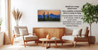 a living room with a wooden coffee table, two white armchairs, and a framed landscape painting of a desert scene hanging on the wall.